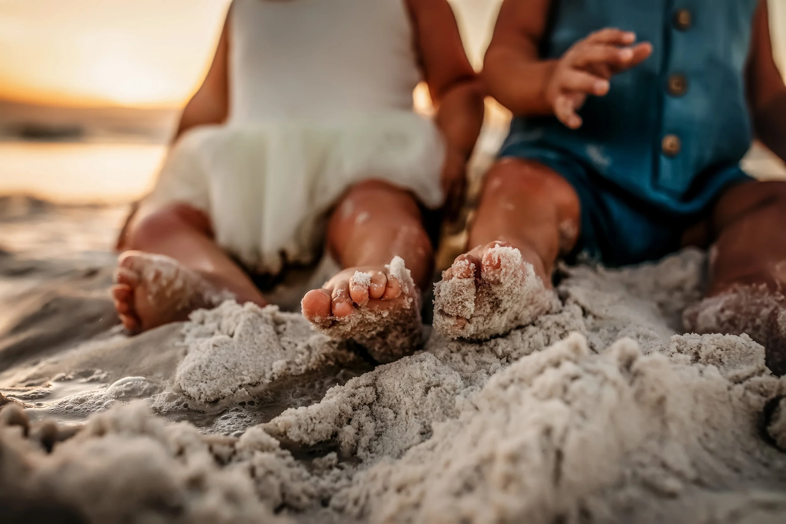 Close-up of toddlers’ sandy feet sitting at the shoreline during a 30A sunset family photography session
