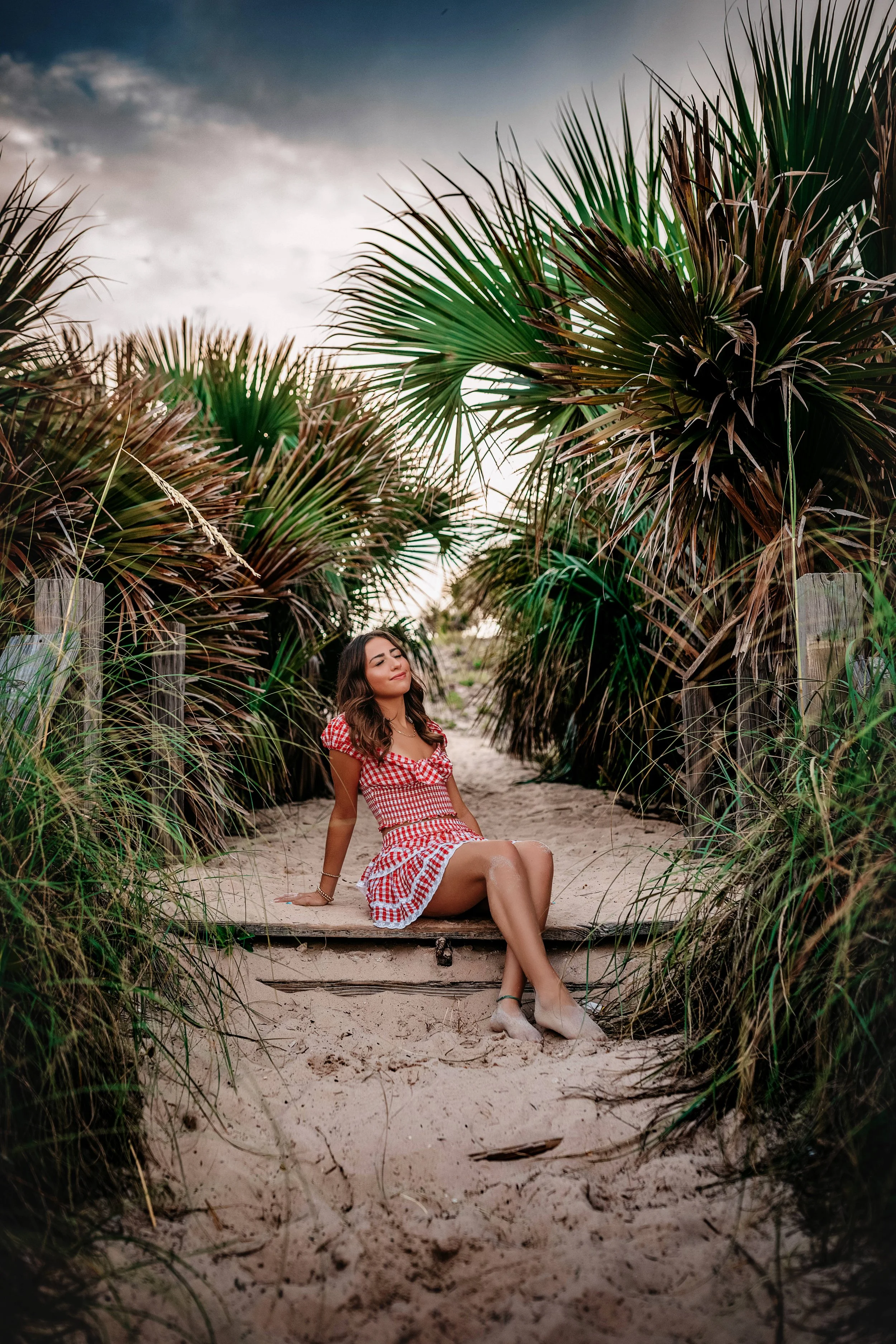 High school senior walking through sand dunes with palm trees in Panama City Beach.