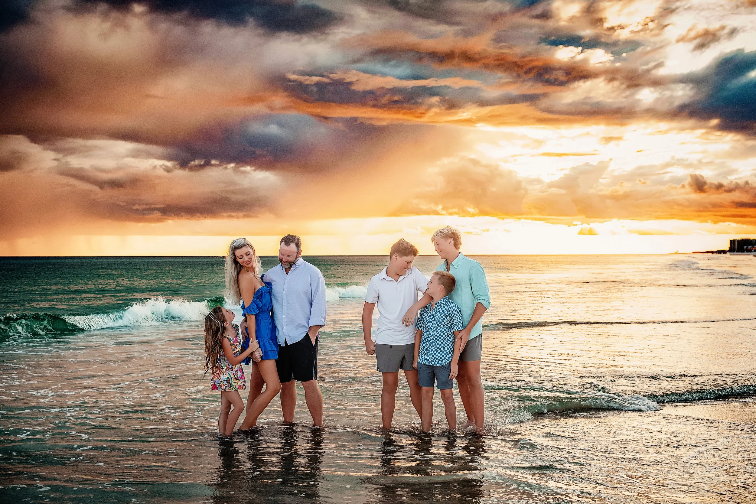 Family standing in the shallow water under a vibrant sunset sky at Blue Mountain Beach.