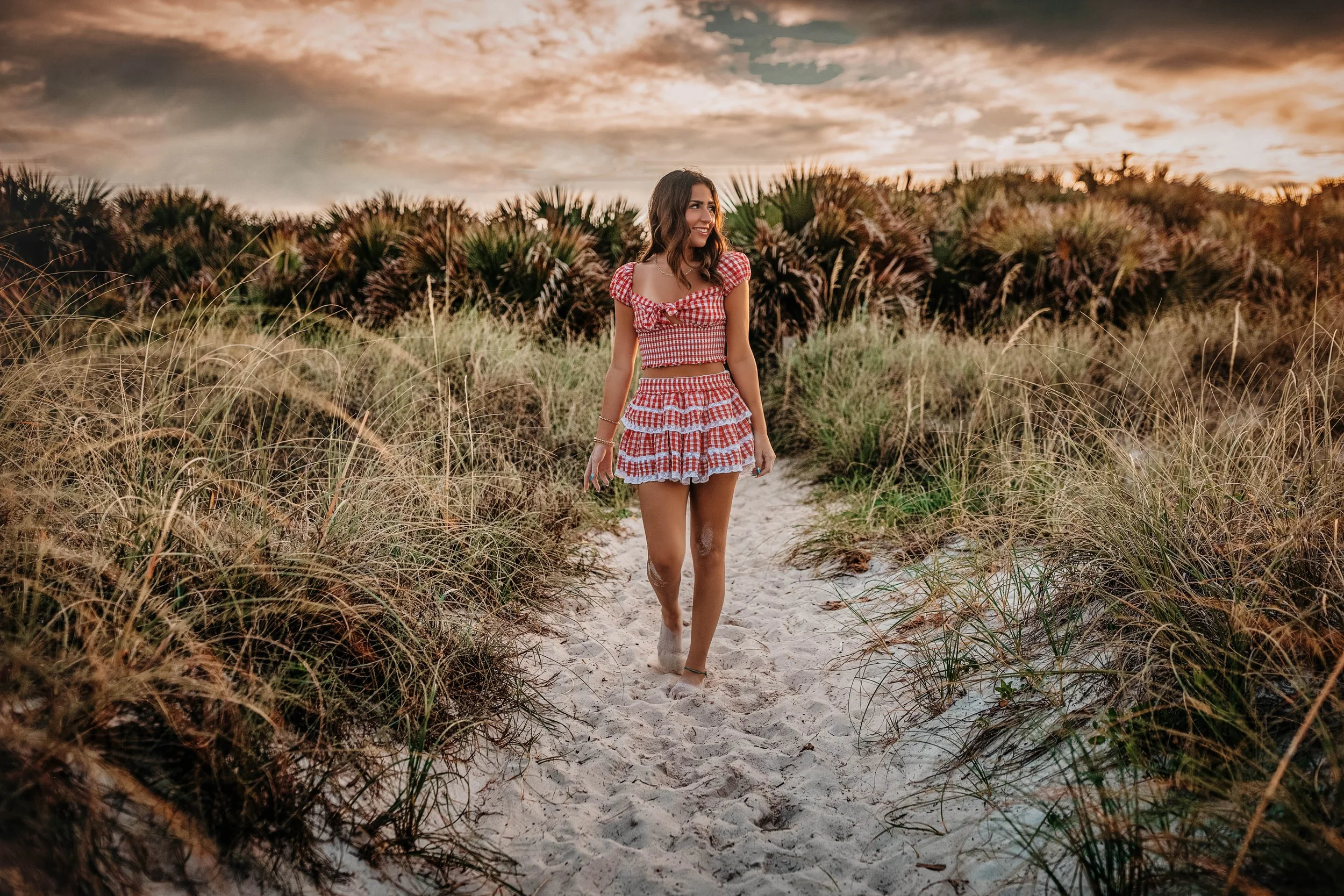 Highschool senior girl walking in between the dune pathway at inlet beach during her 30A Senior session.