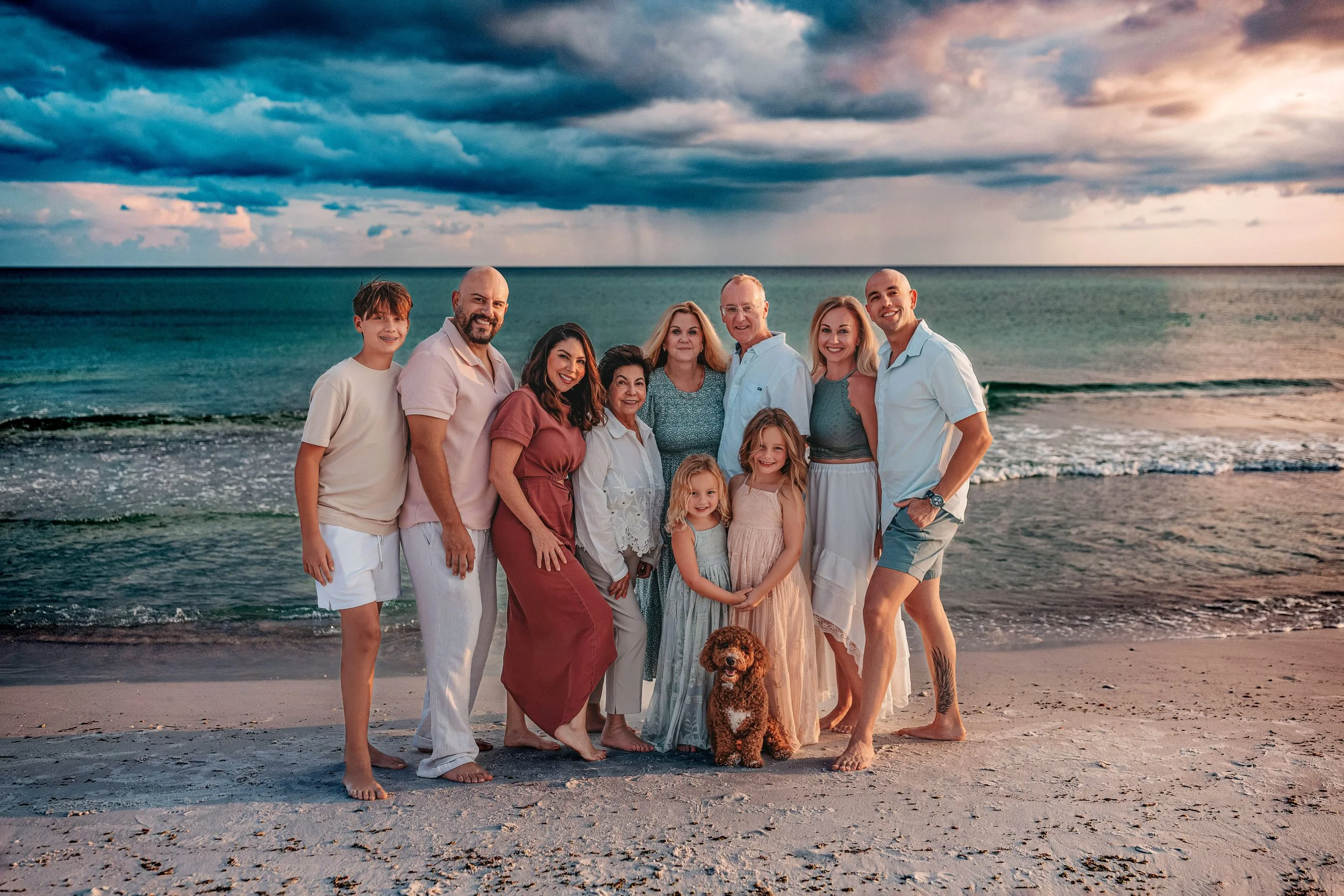 Family of 11 standing against the emerald water as they all  smile and embrace on the shore line on the Seaside Fl beach during their family reunion beach session at sunset 