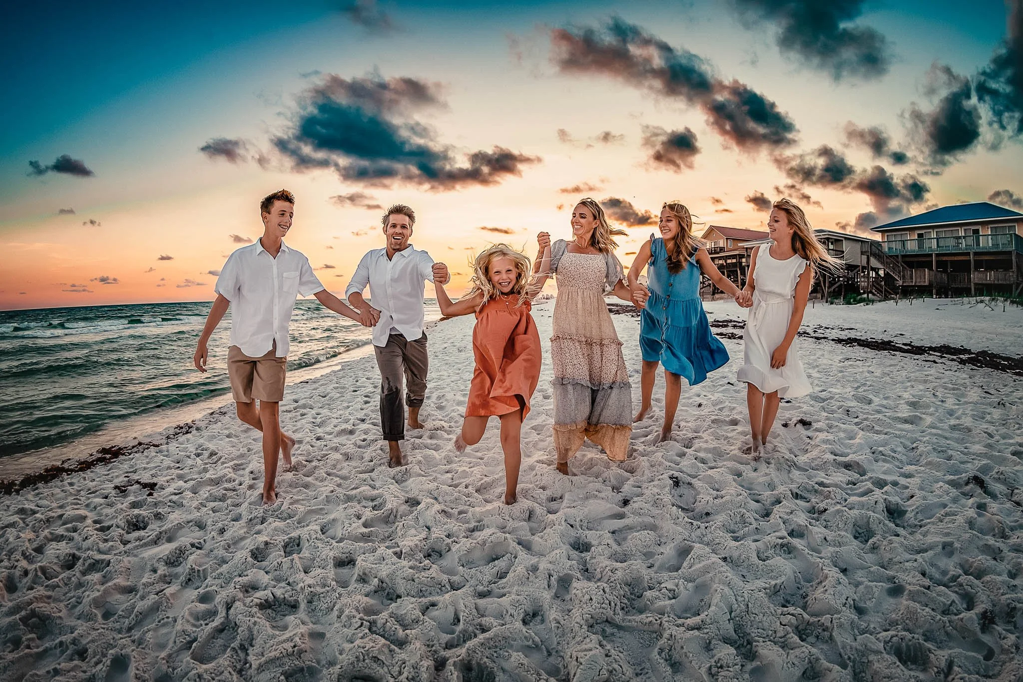 Family of six running along the emerald coast shore line during their family beach session at sunset