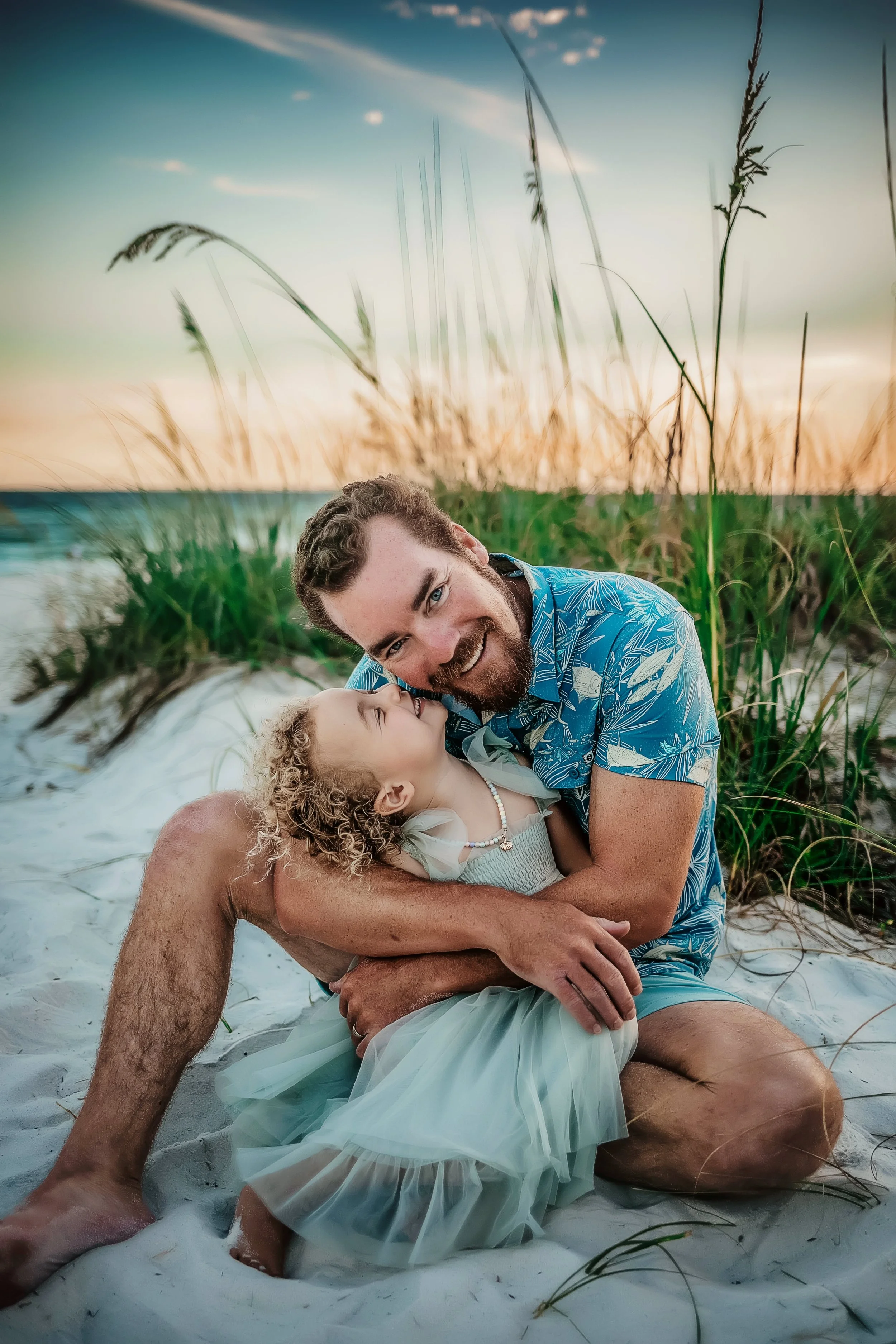 A father hugging his young daughter in a mint green dress during a sunset family portrait session at Santa Rosa Beach, Florida.
