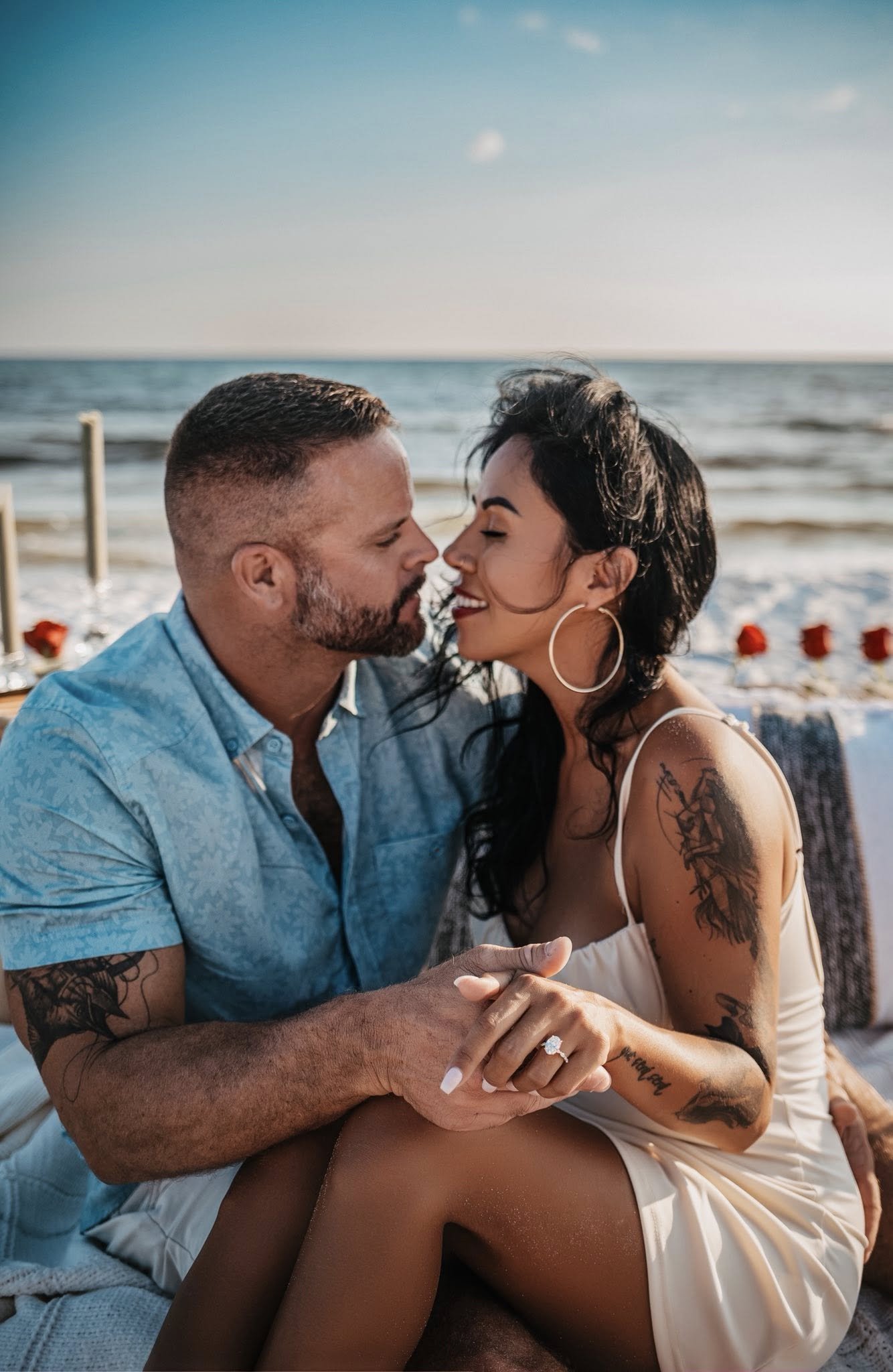 30A Florida couples beach photography session at sunset — man in light blue shirt and tattooed woman in white dress sharing an intimate moment with Gulf Coast ocean wave