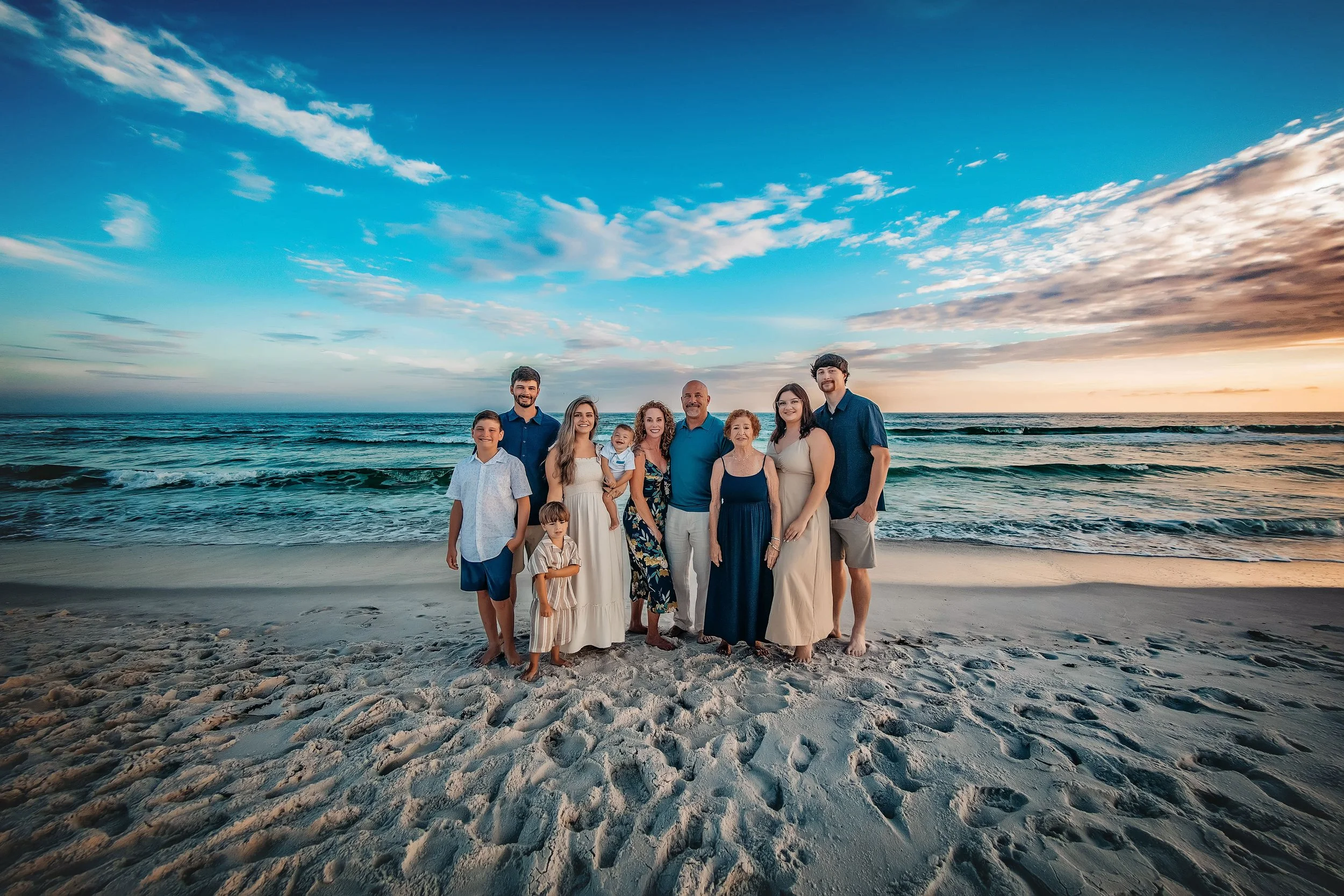 Multi-generational family portrait of fifteen people standing in the emerald Gulf surf at sunset in Destin, Florida.