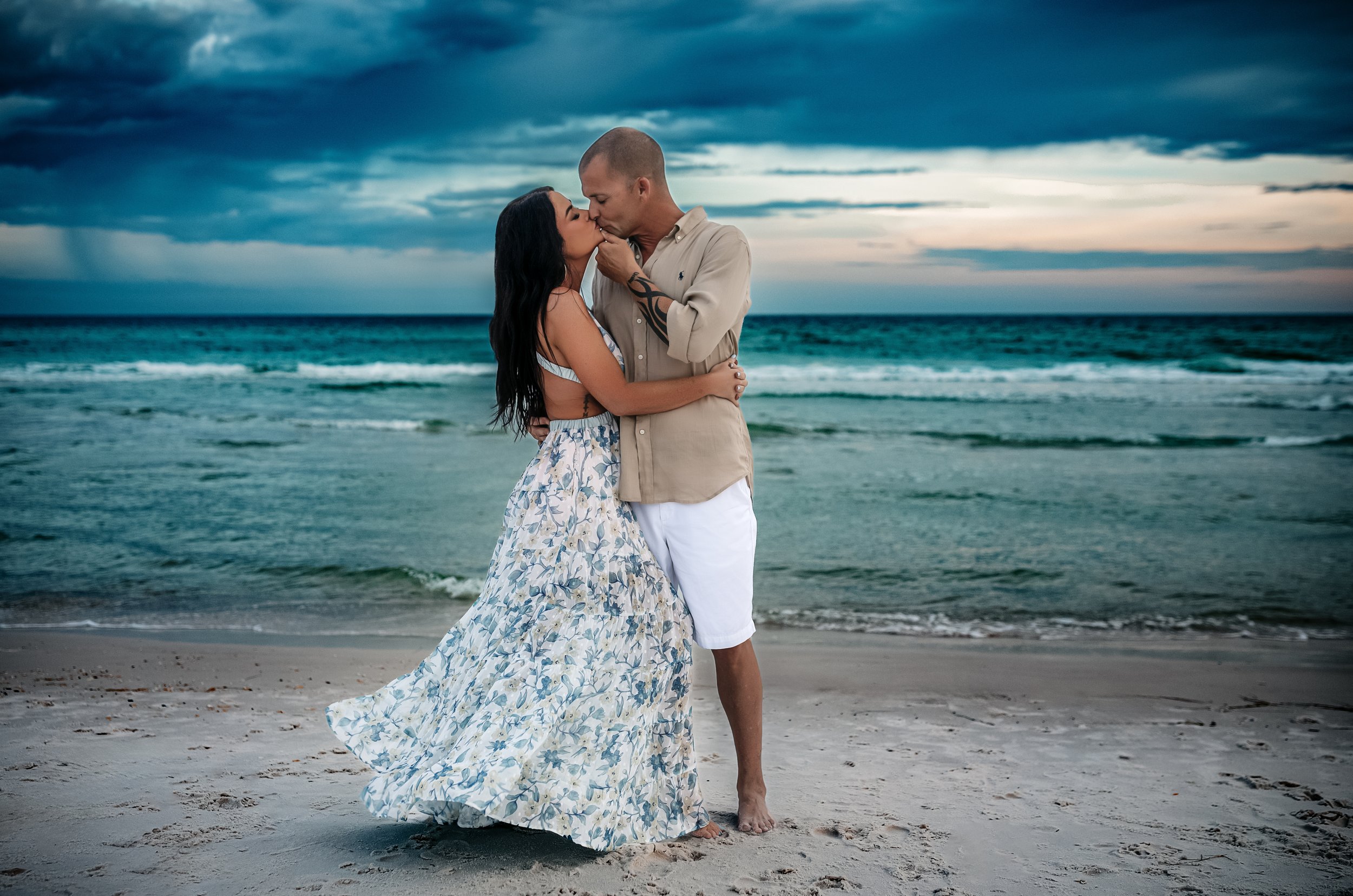 ouple kissing on 30A beach at sunset — woman in flowing blue floral maxi dress, man in khaki linen shirt and white shorts — Destin Florida beach photographer