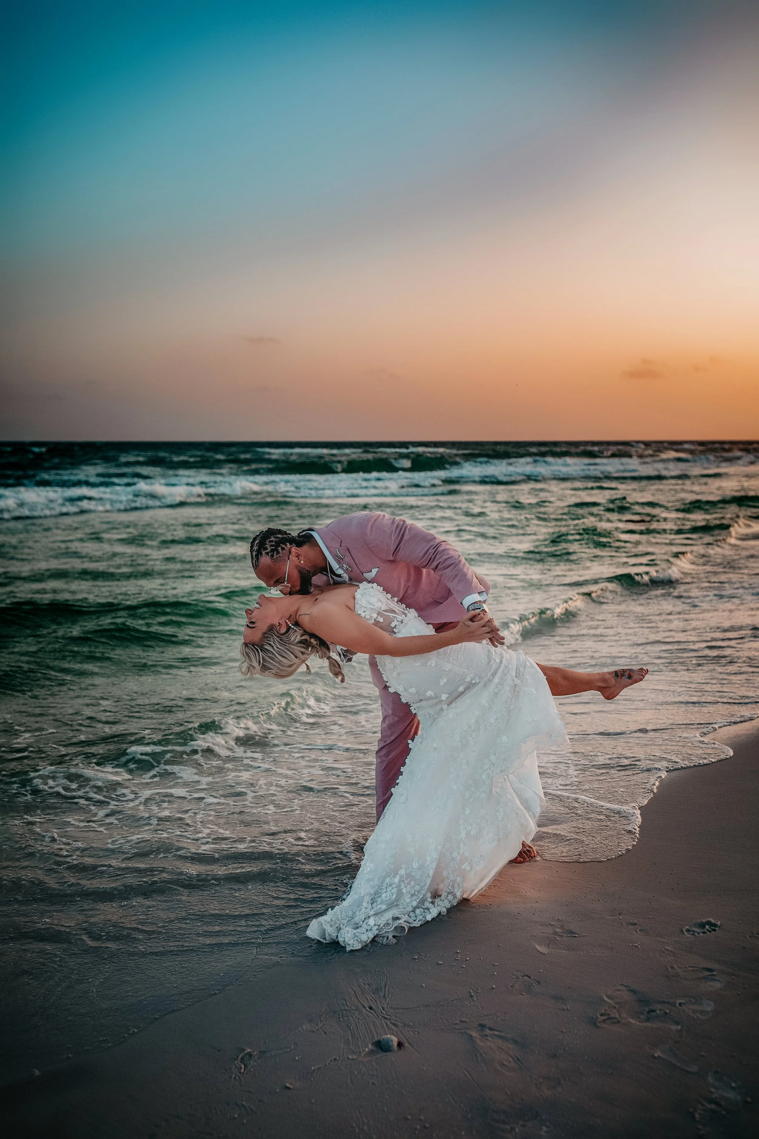 A bride being dipped by her groom during their wedding taking place at sunset in Panama City Beach
