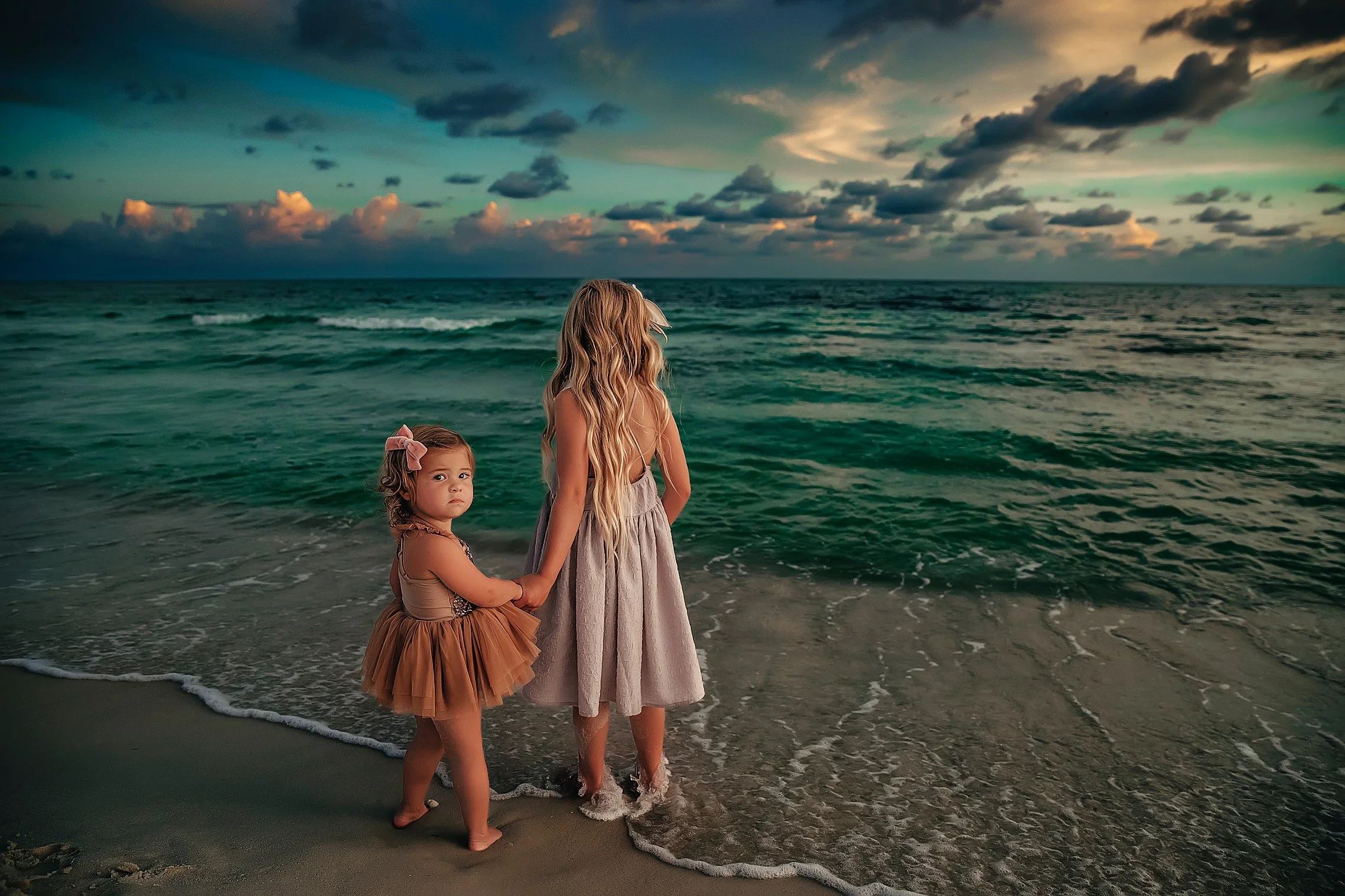 Two young girls in beach dresses standing along the shoreline during a family session near Rosemary Beach.