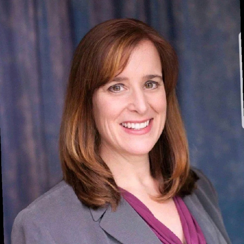 A white woman with brown hair  in a gray blazer smiling
