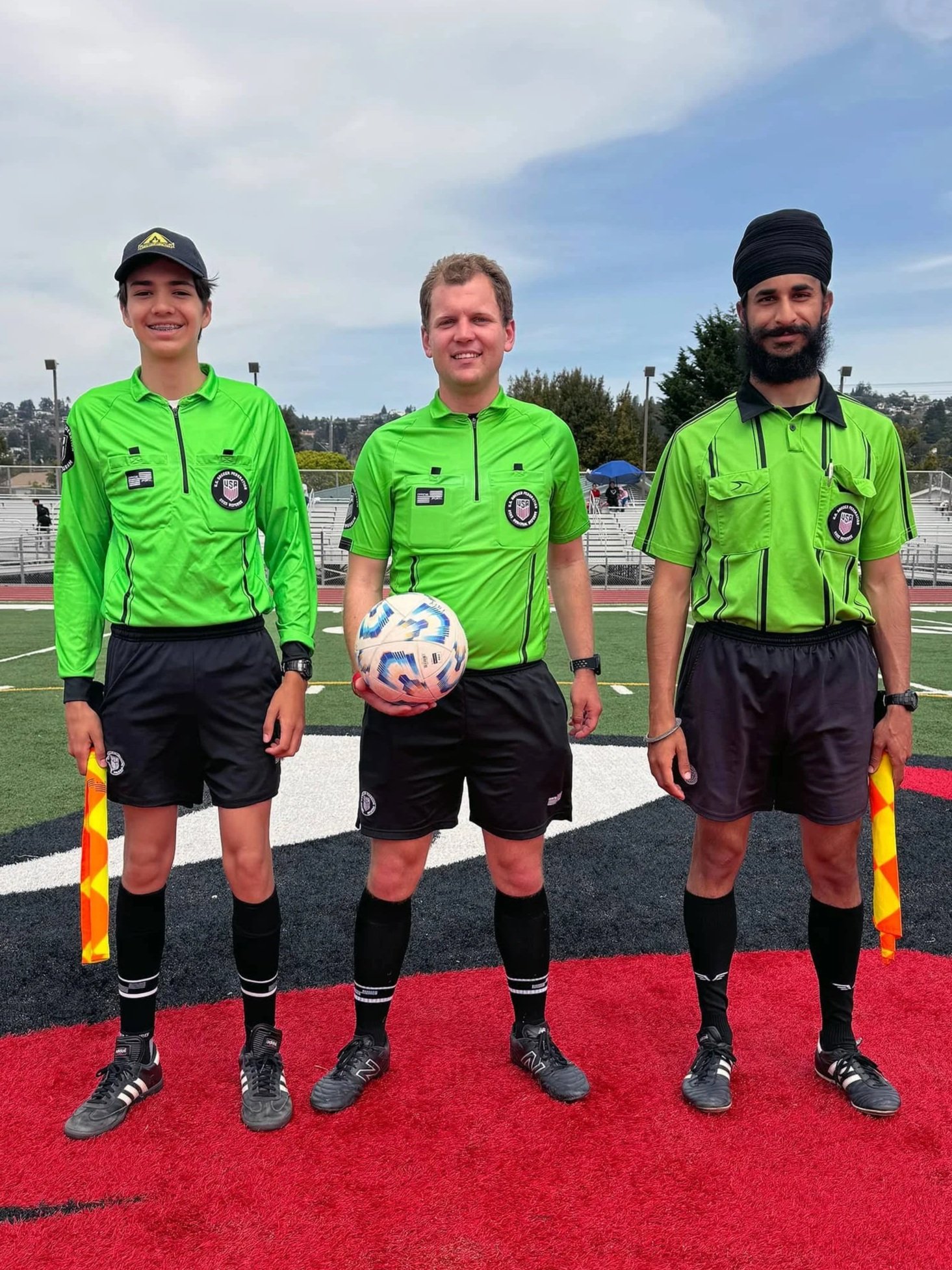Youth soccer referees stand on the field before a match at an Eastshore Alliance FC game, representing referee development and match officiating.
