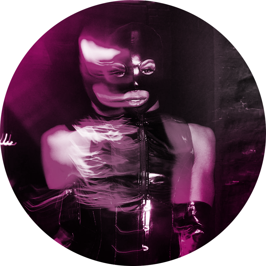 A man stares at the viewer with pride, sensuality & confidence, wearing a latex bodysuit, mask & long gloves. He has long eyelashes & bold eyeshadow, with half the frame artistically blurred.