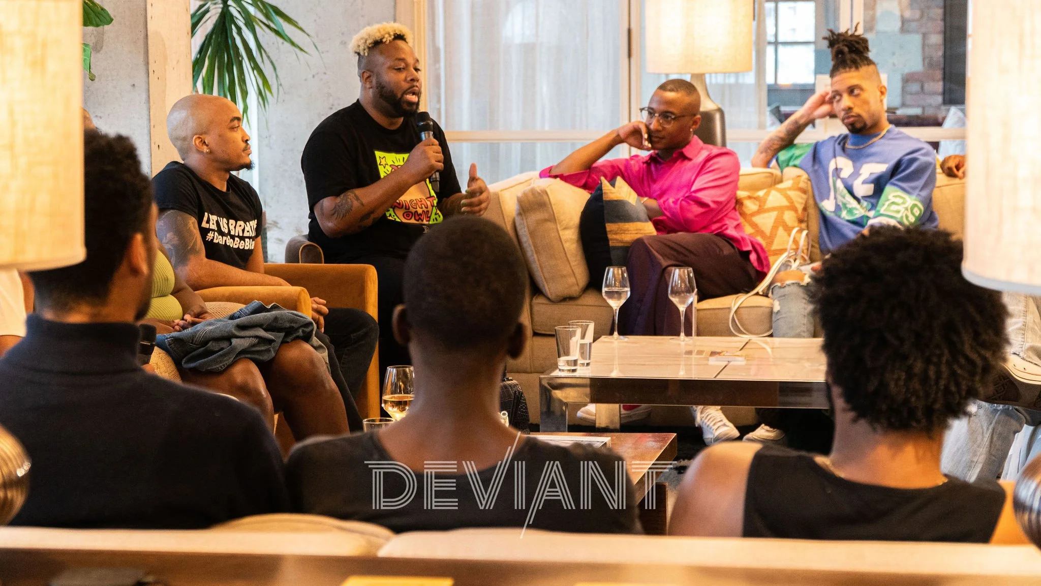 A Cocktails & Conversation event called "Safe Spaces" hosted by Deviant Society. A group of people are seated in comfortable couches & chairs, surrounding a panel about mental health.