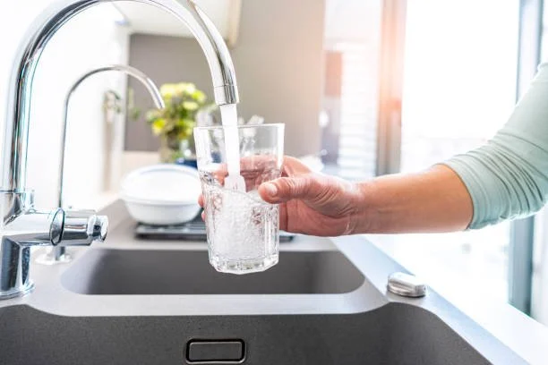 Person filling a glass with water from a faucet in a kitchen.
