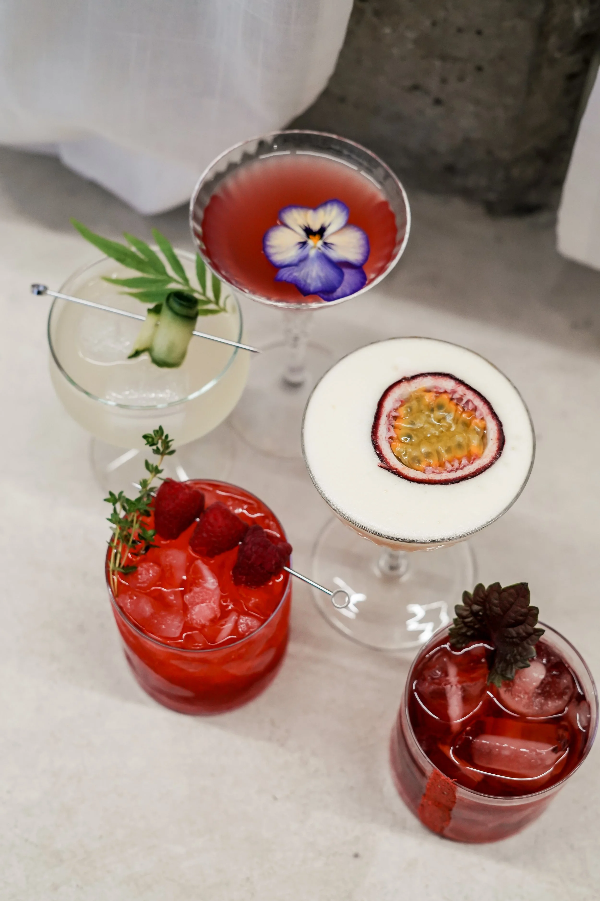 Array of colorful cocktails garnished with fruits and herbs on a table.