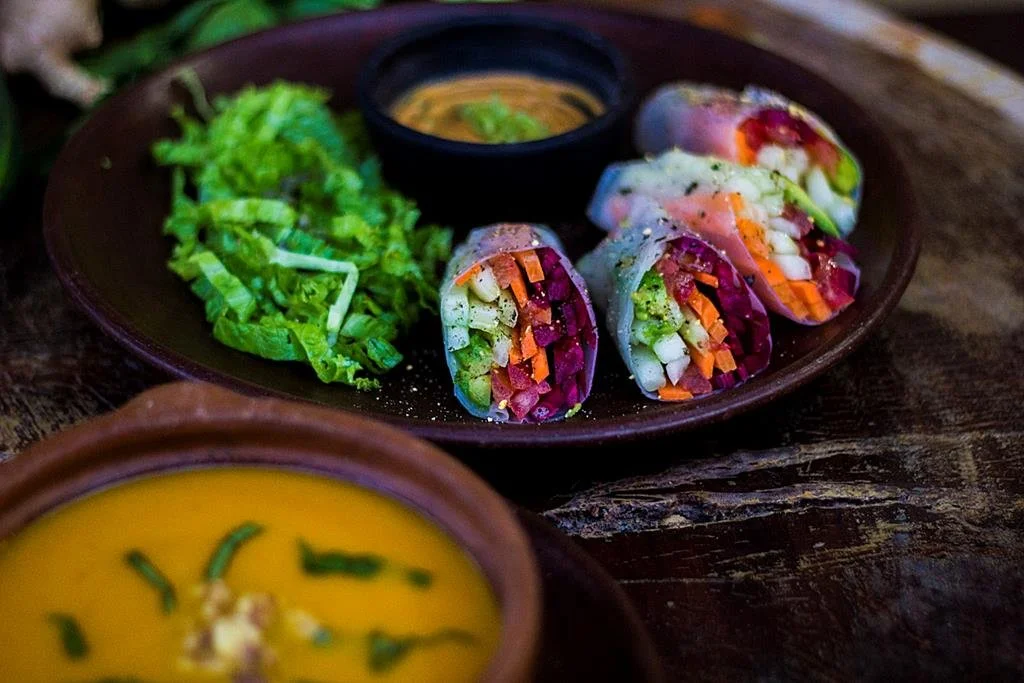 Colorful plant-based detox meal with vegetable rolls, fresh greens, and soup served on a dark wooden table – vegan cuisine at Nicaragua yoga retreat