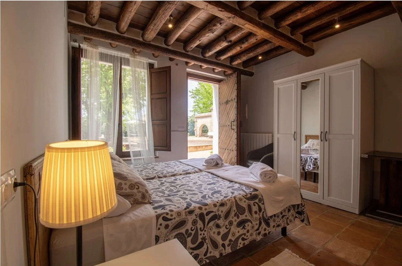 Spacious and elegantly decorated bedroom at Casería de Milán, a 16th-century Andalusian estate near Granada, Spain, featuring vintage furnishings, a cozy fireplace, and classic decor, offering a comfortable stay during the retreat.