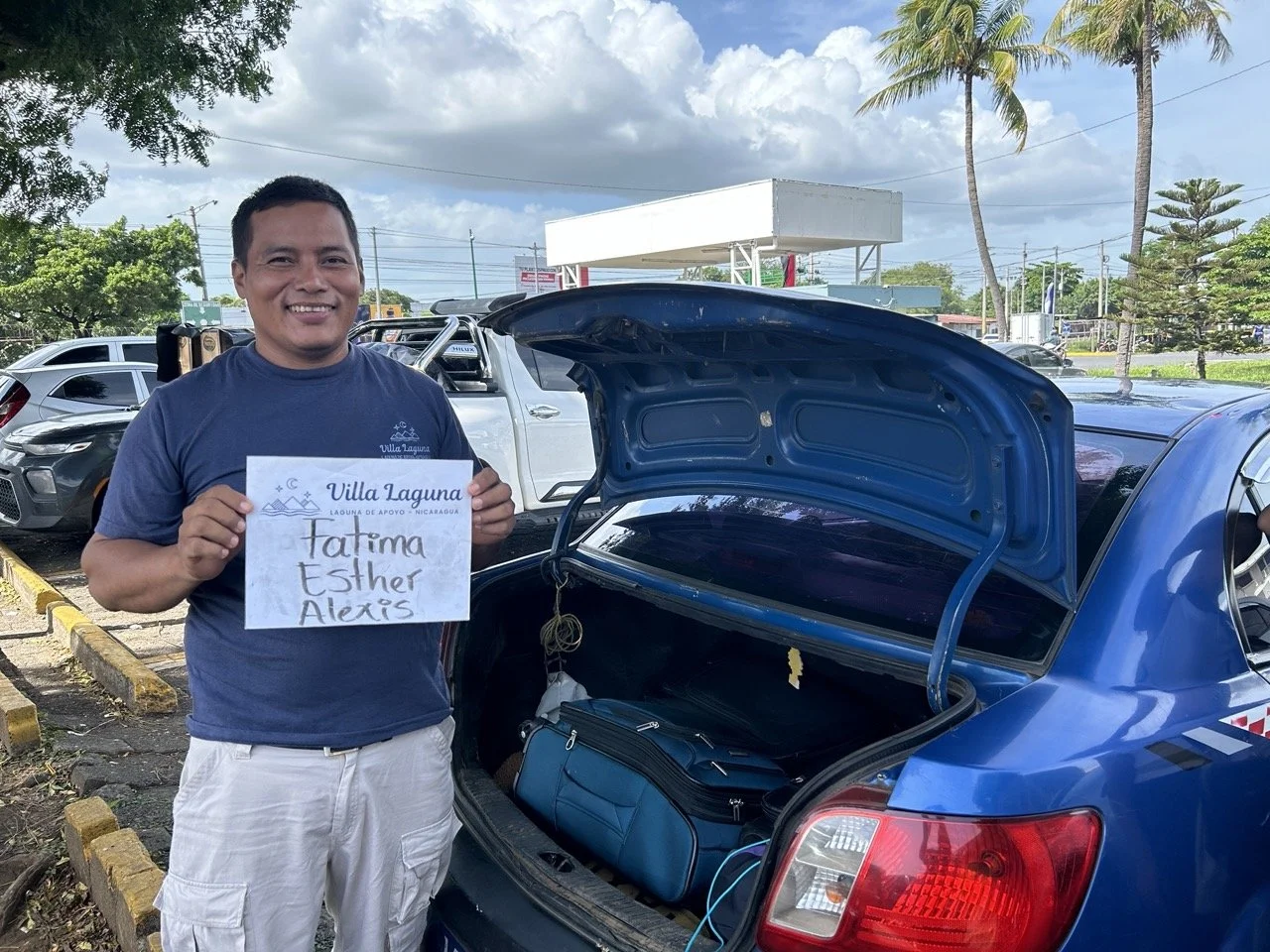 Villa Laguna retreat driver holding a guest welcome sign next to a blue car with open trunk, ready for airport pickup in Nicaragua