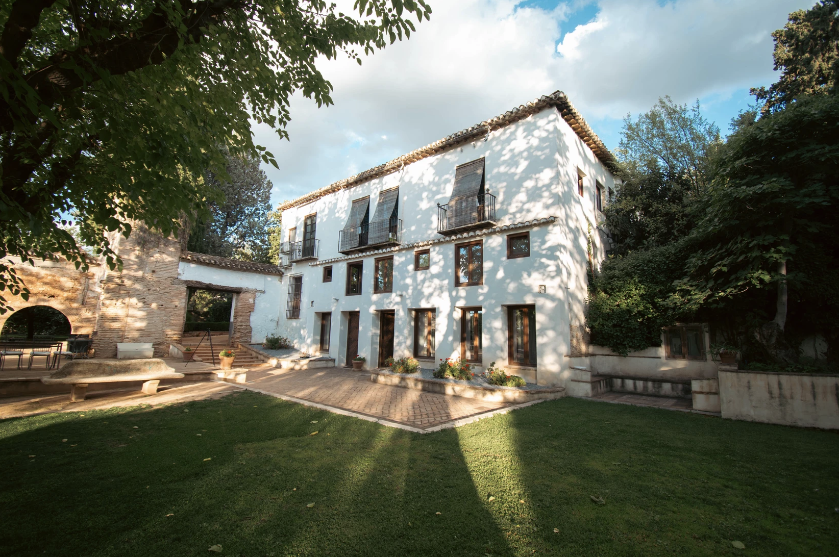 Exterior view of Casería de Milán, a beautiful 16th-century Andalusian estate surrounded by lush greenery, featuring whitewashed walls and traditional architecture, serving as the exclusive venue for retreats in Granada, Spain.