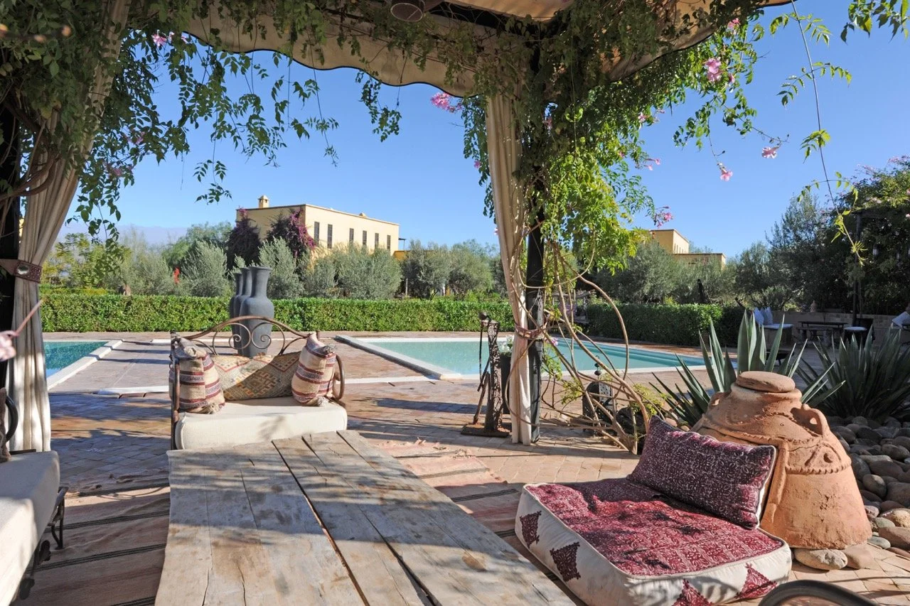 Shaded terrace with Moroccan seating overlooking the pool and gardens at the countryside retreat venue near Marrakech.