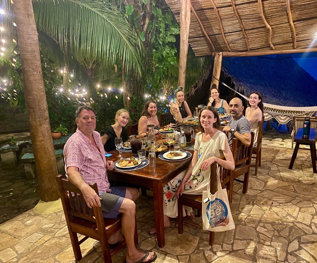 Retreat guests enjoying a plant-based dinner under a thatched roof at Villa Laguna, surrounded by tropical greenery and soft evening lights.
