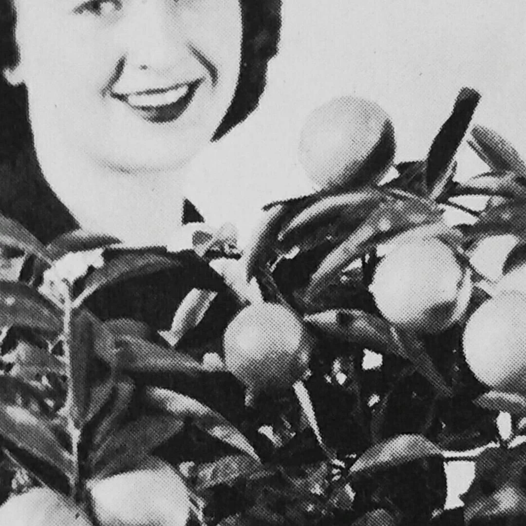 Black and white halftone image of a woman smiling seated behind a citrus plant.