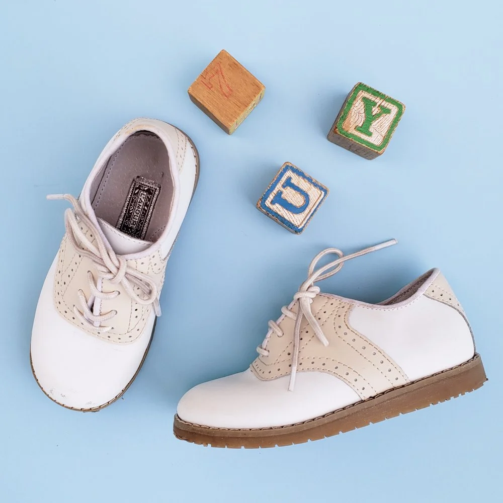 Photo of children's oxford shoes with wooden blocks against a blue background.