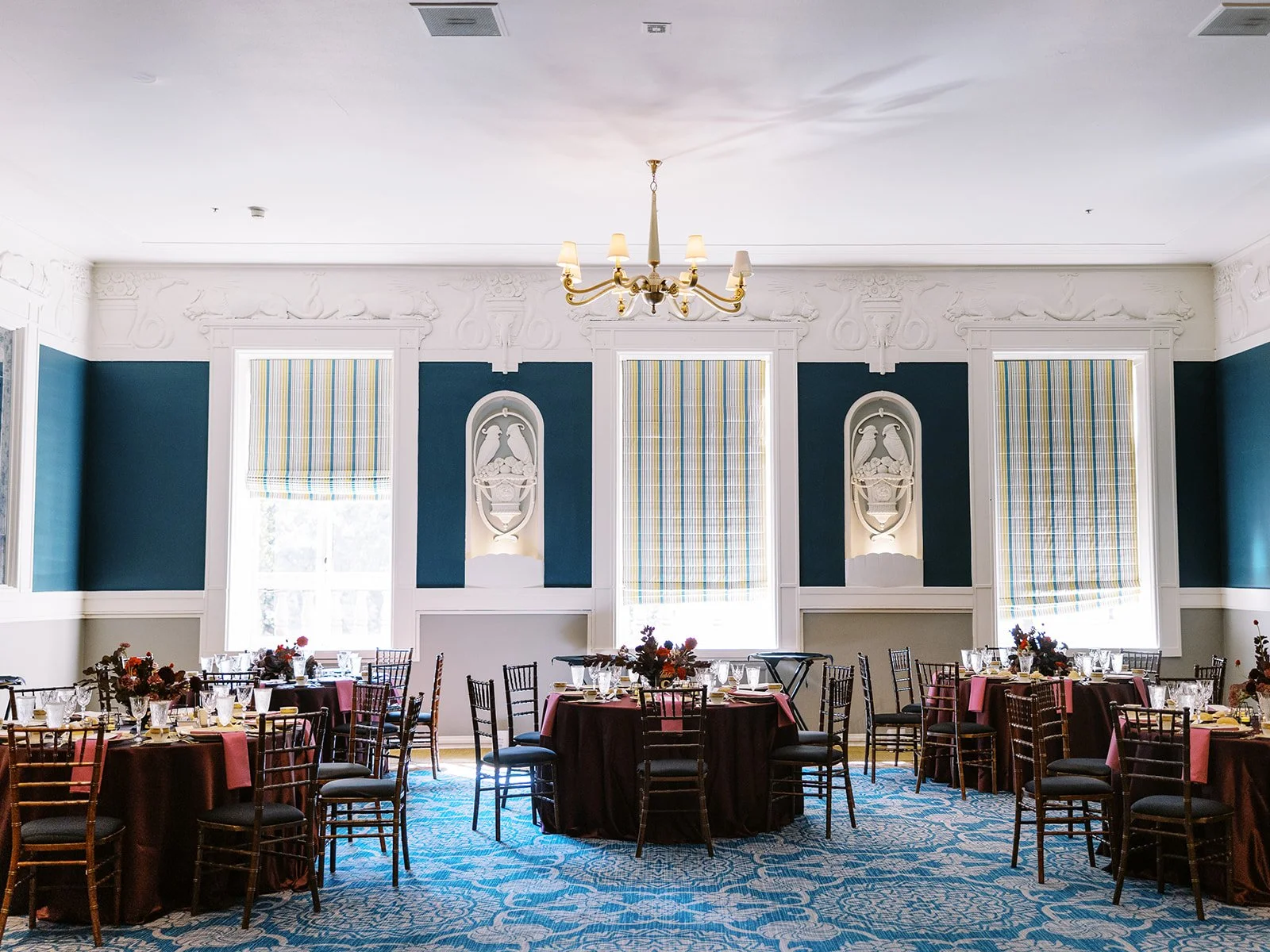 Round reception tables with burgundy linens arranged in bright ballroom with tall windows at the Sentinel Hotel in Portland.