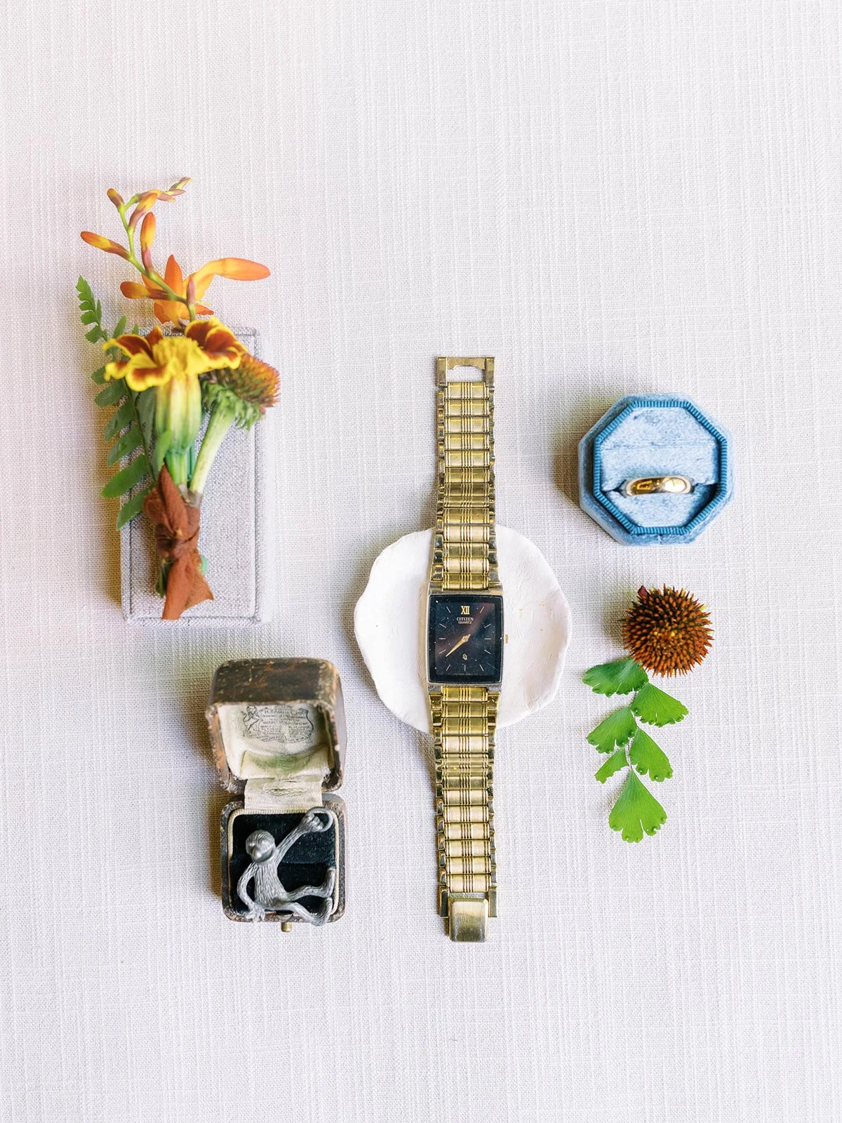 Groom’s details with boutonniere, gold watch, ring, and cufflinks on neutral background