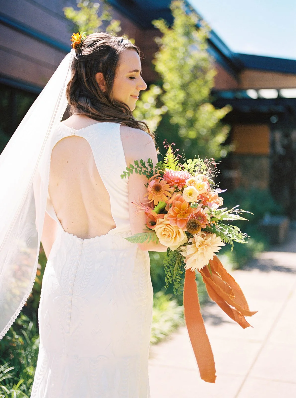 Bride turned slightly away showing open-back dress and holding bright floral bouquet