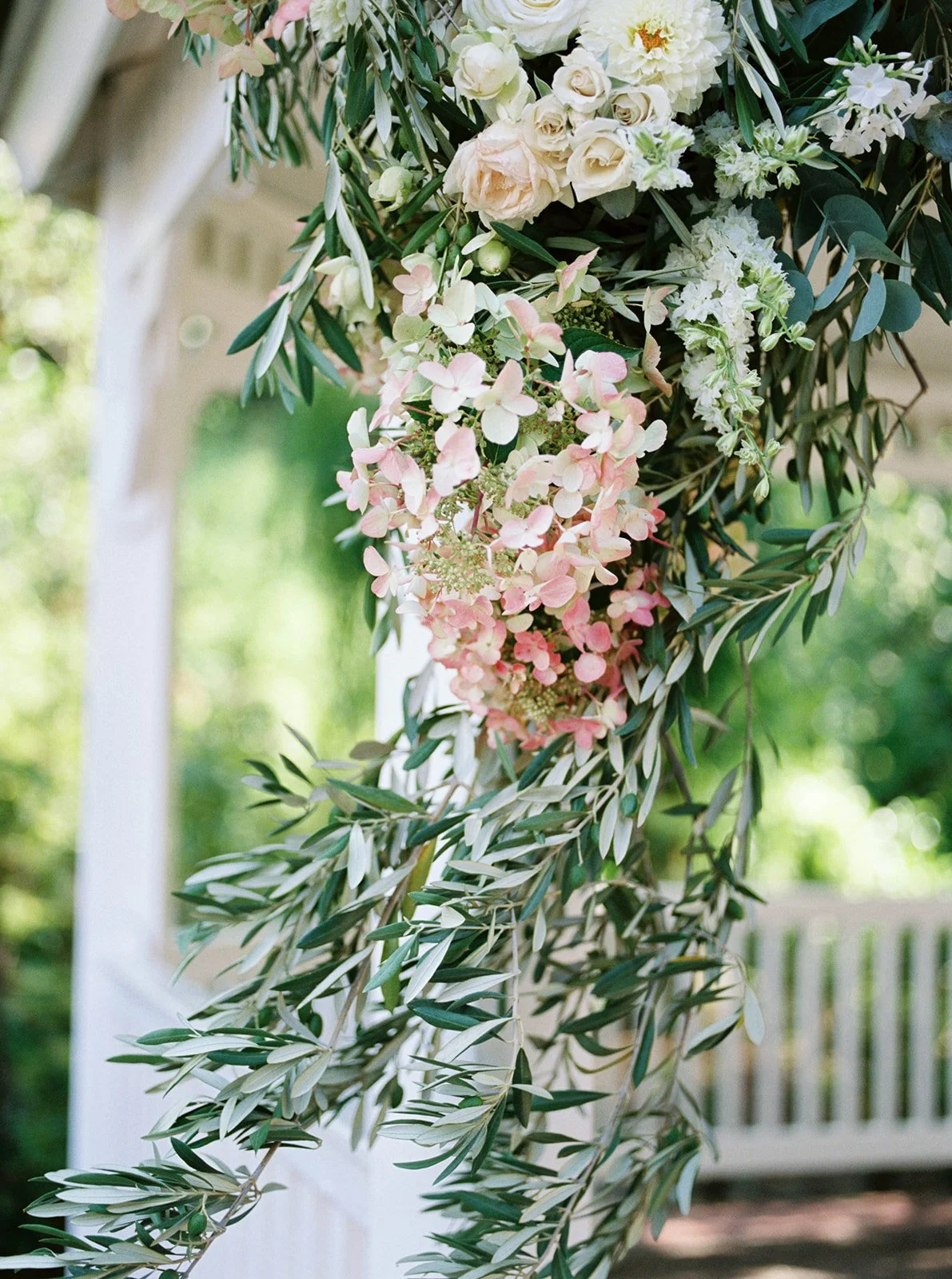 Romantic blush and white floral ceremony arrangement with greenery cascading from Abigail’s Garden gazebo.
