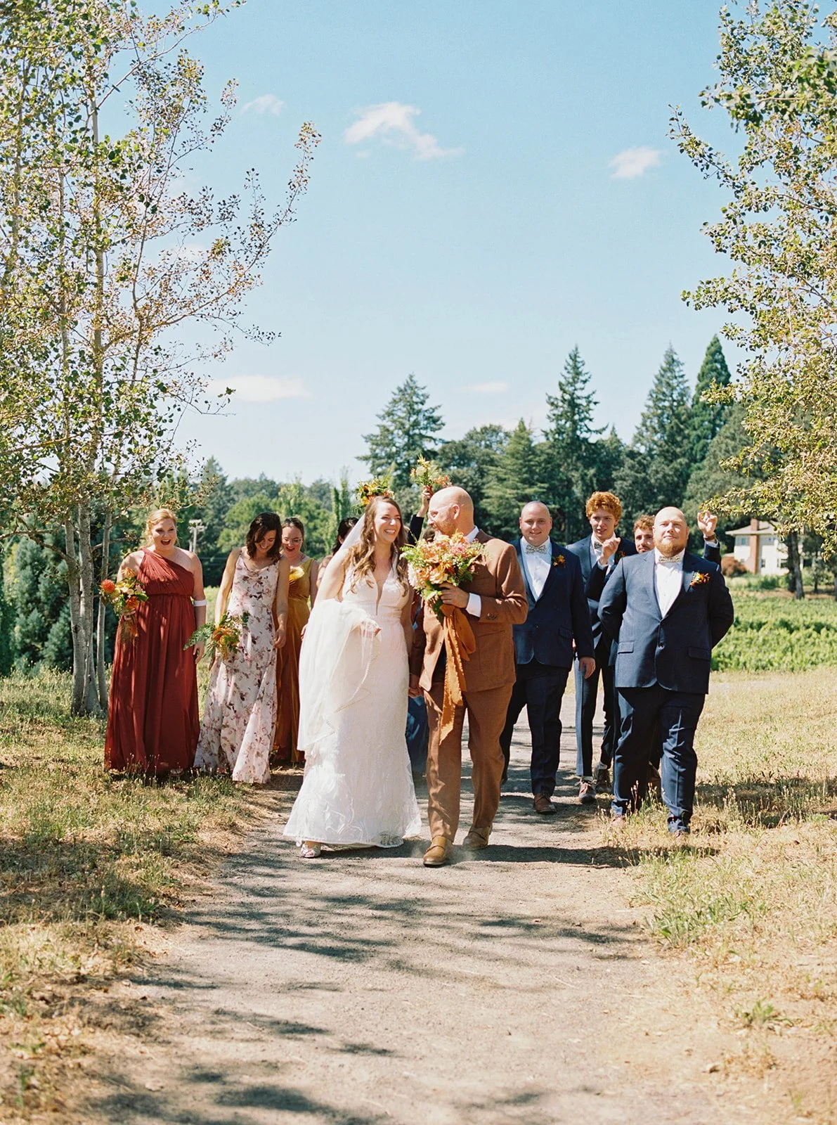 Wedding party walking together on path outdoors, bride and groom leading group