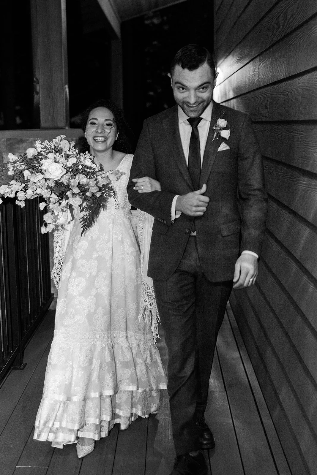 Black-and-white portrait of the newlyweds walking arm in arm after their nighttime wedding ceremony.