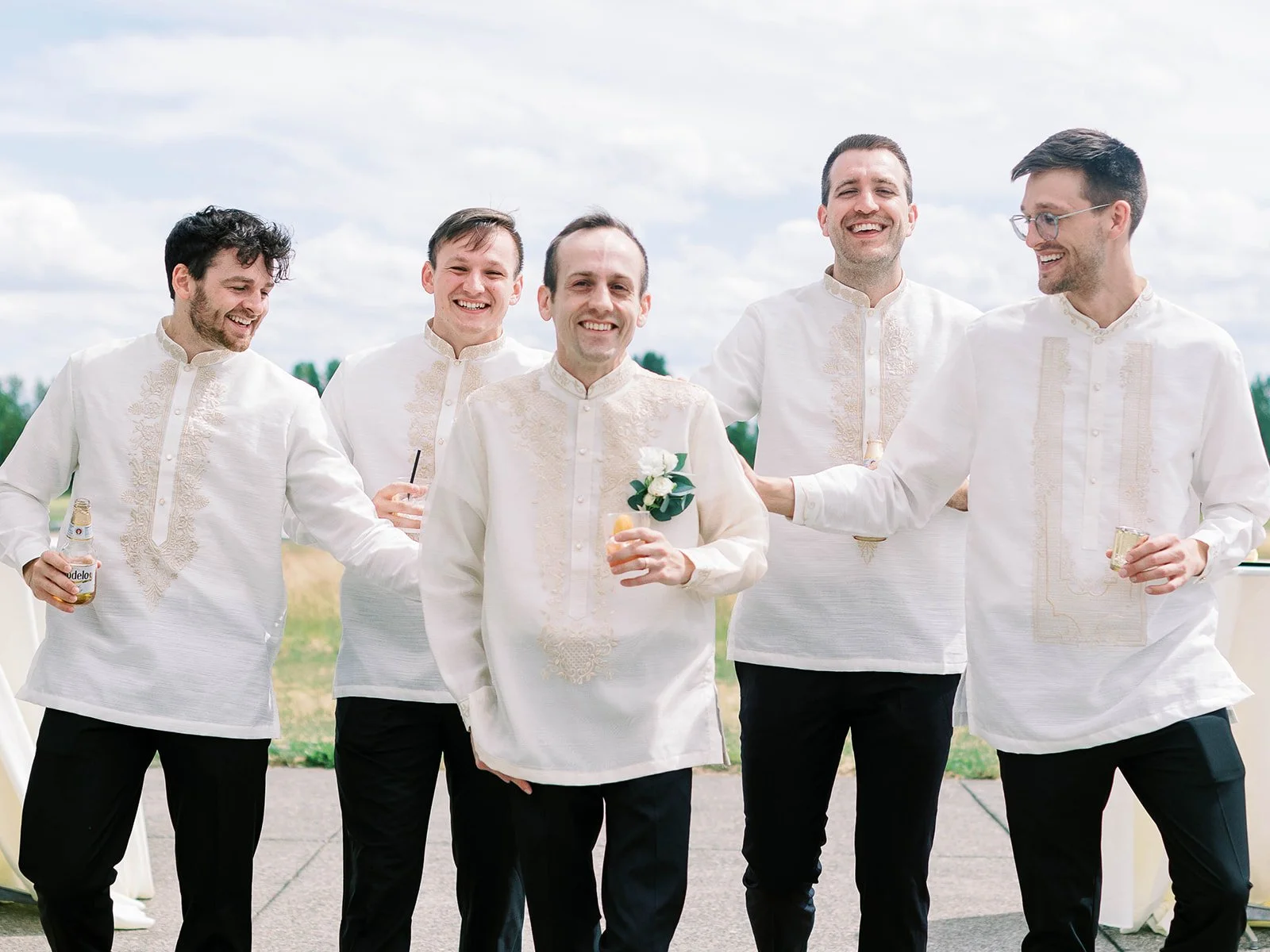 Groom and four groomsmen laughing together outdoors in matching white embroidered barong tagalog shirts and black trousers at Pearson Airfield
