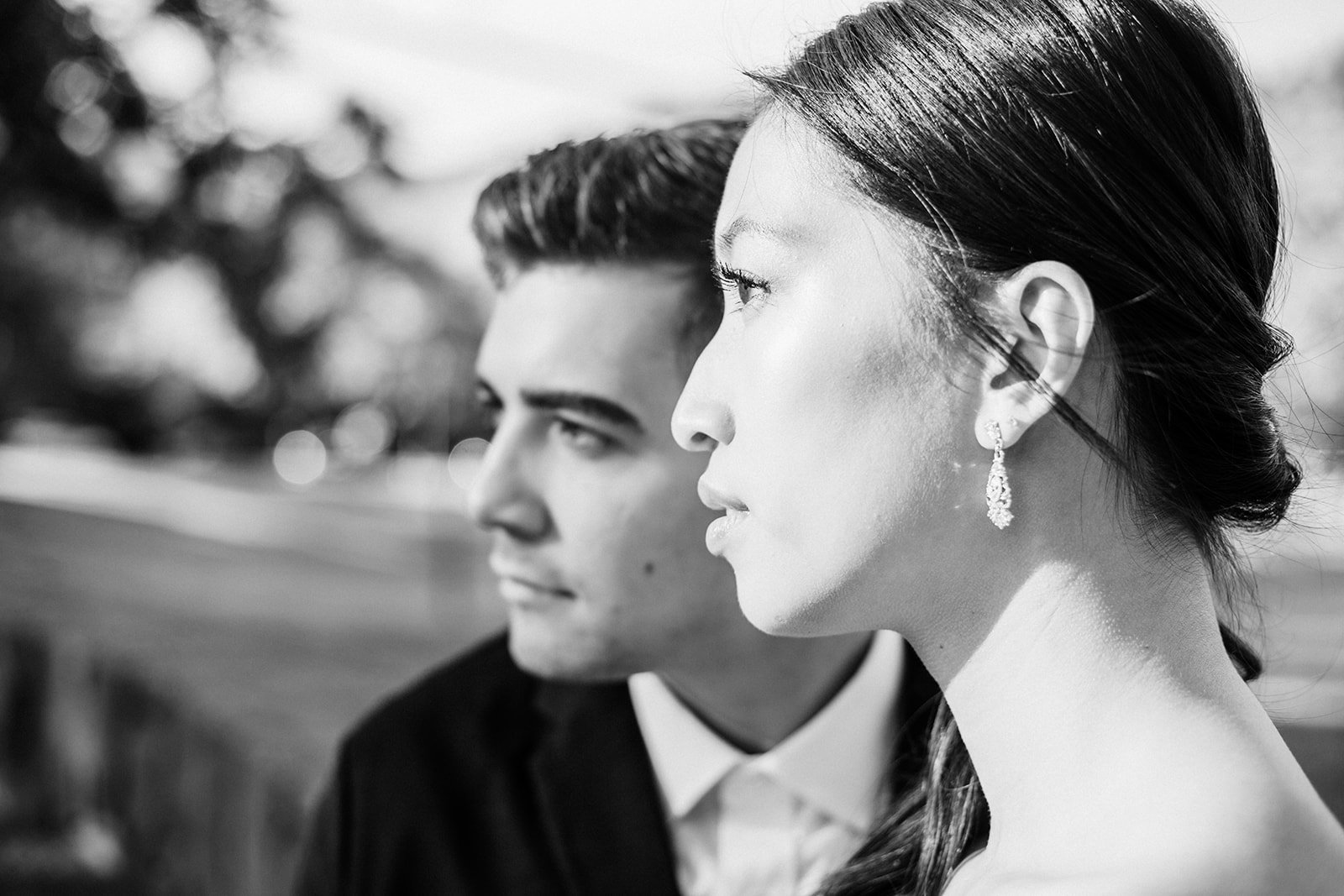 Black-and-white profile portrait of couple outdoors, bride with earrings and groom in suit looking ahead