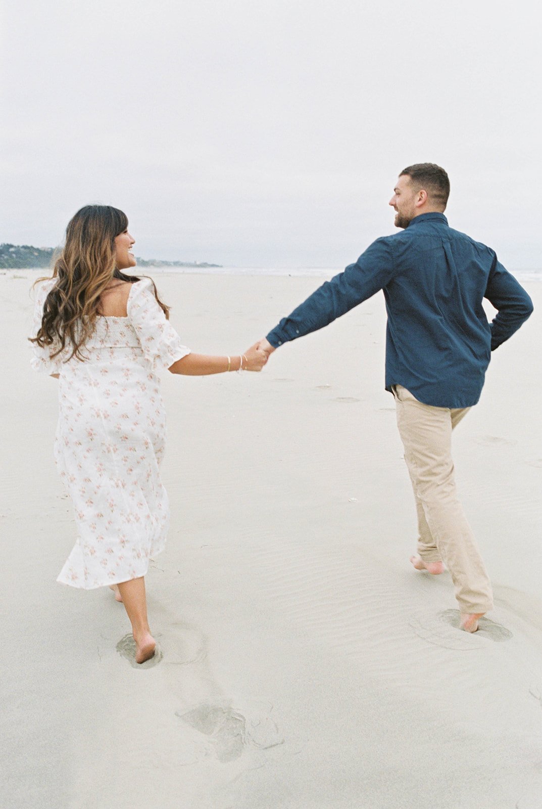 Couple running hand in hand across sandy beach toward ocean shoreline