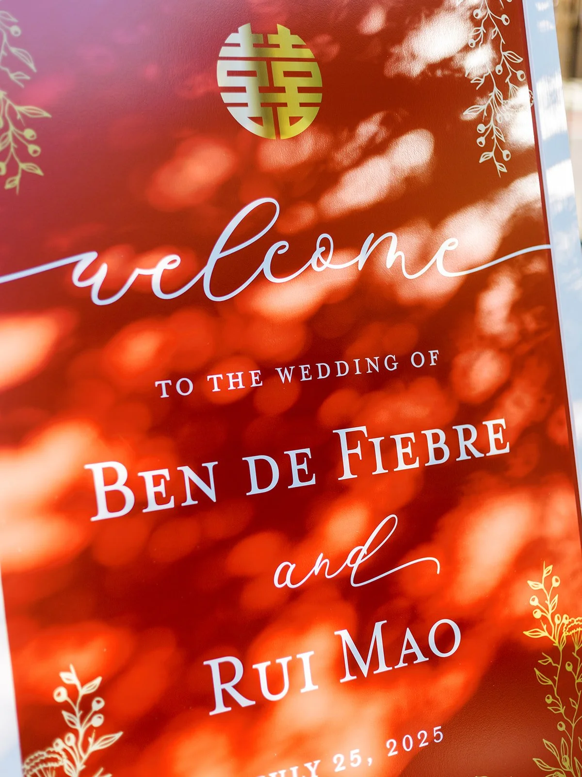 Close-up of the red and gold wedding welcome sign reading "Welcome to the Wedding of Ben de Fiebre and Rui Mao, July 25, 2025," with a gold double-happiness symbol.