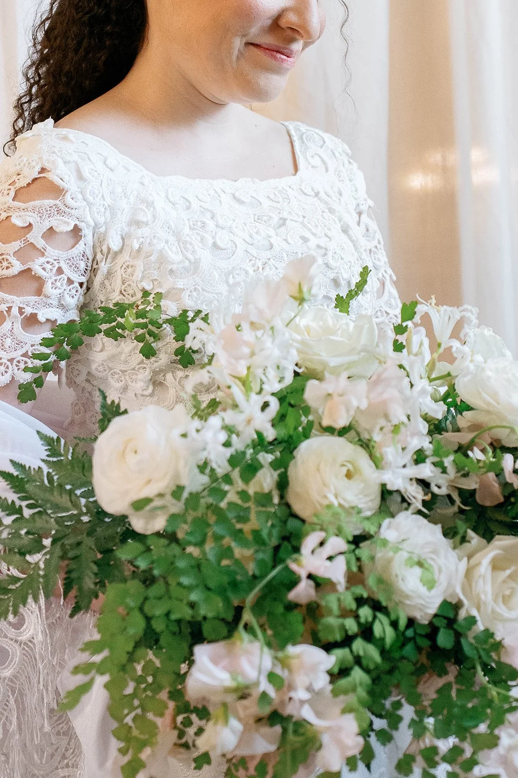 Close-up of the bride’s vintage lace gown and cascading bouquet of white flowers and greenery.