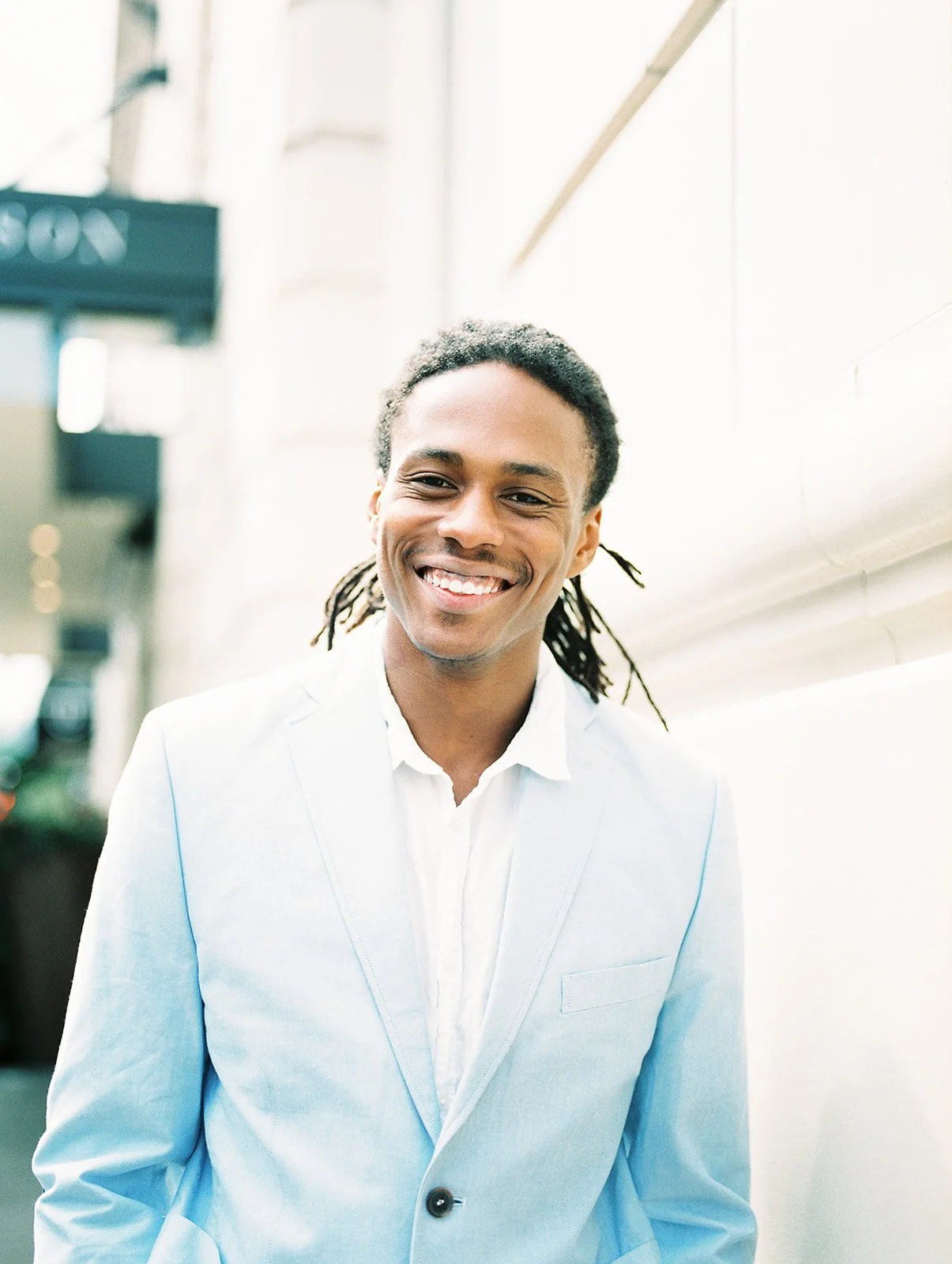 Smiling man in light blue blazer standing against building wall in downtown Portland