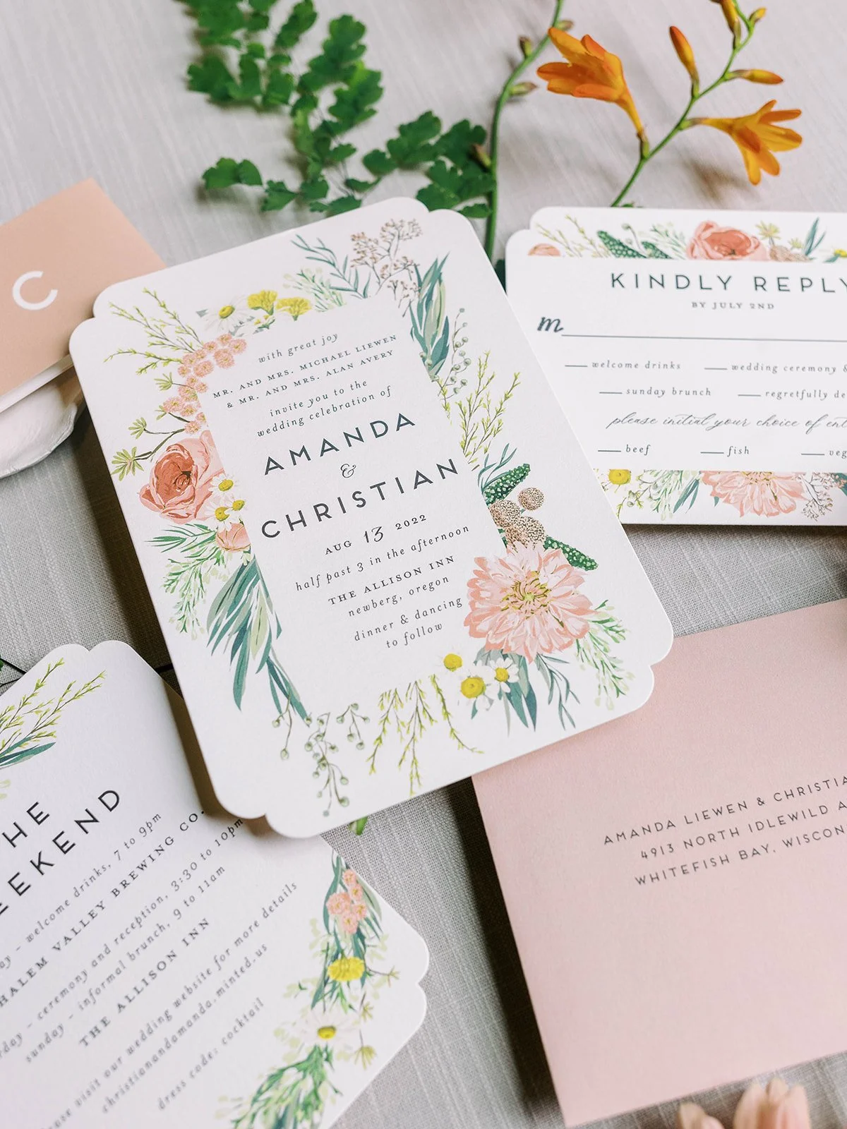 Floral wedding invitation suite with peach, orange and green botanical details arranged beside fresh flowers.