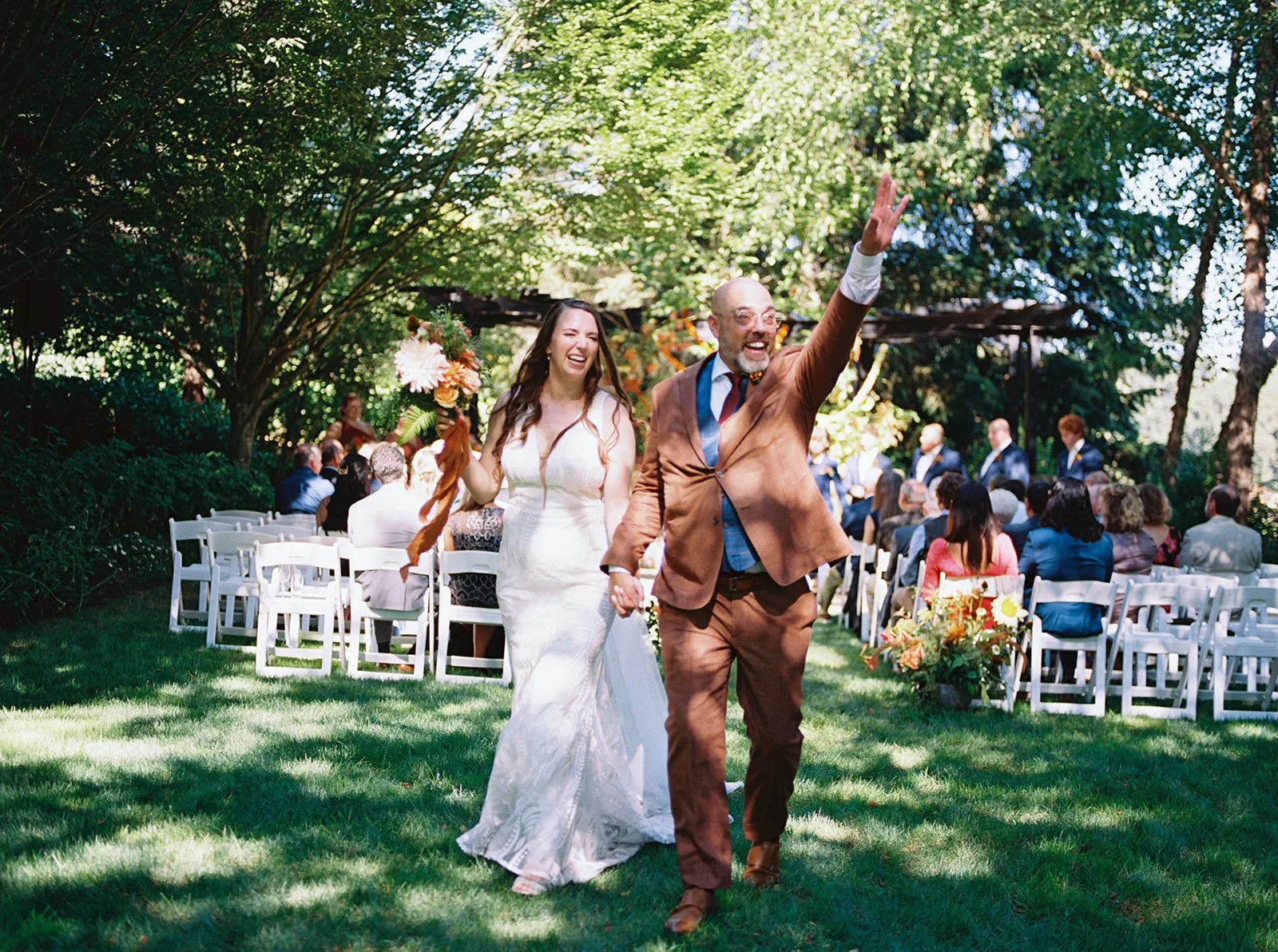 Newlyweds walking hand in hand down the aisle after their outdoor garden wedding ceremony.