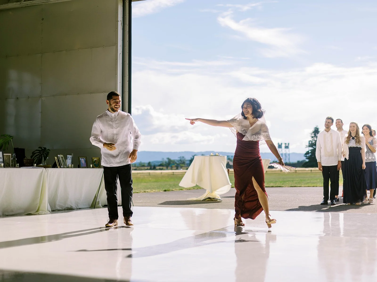 Bridesmaid in a burgundy slit skirt dancing exuberantly on the hangar floor during the reception entrance while guests cheer

