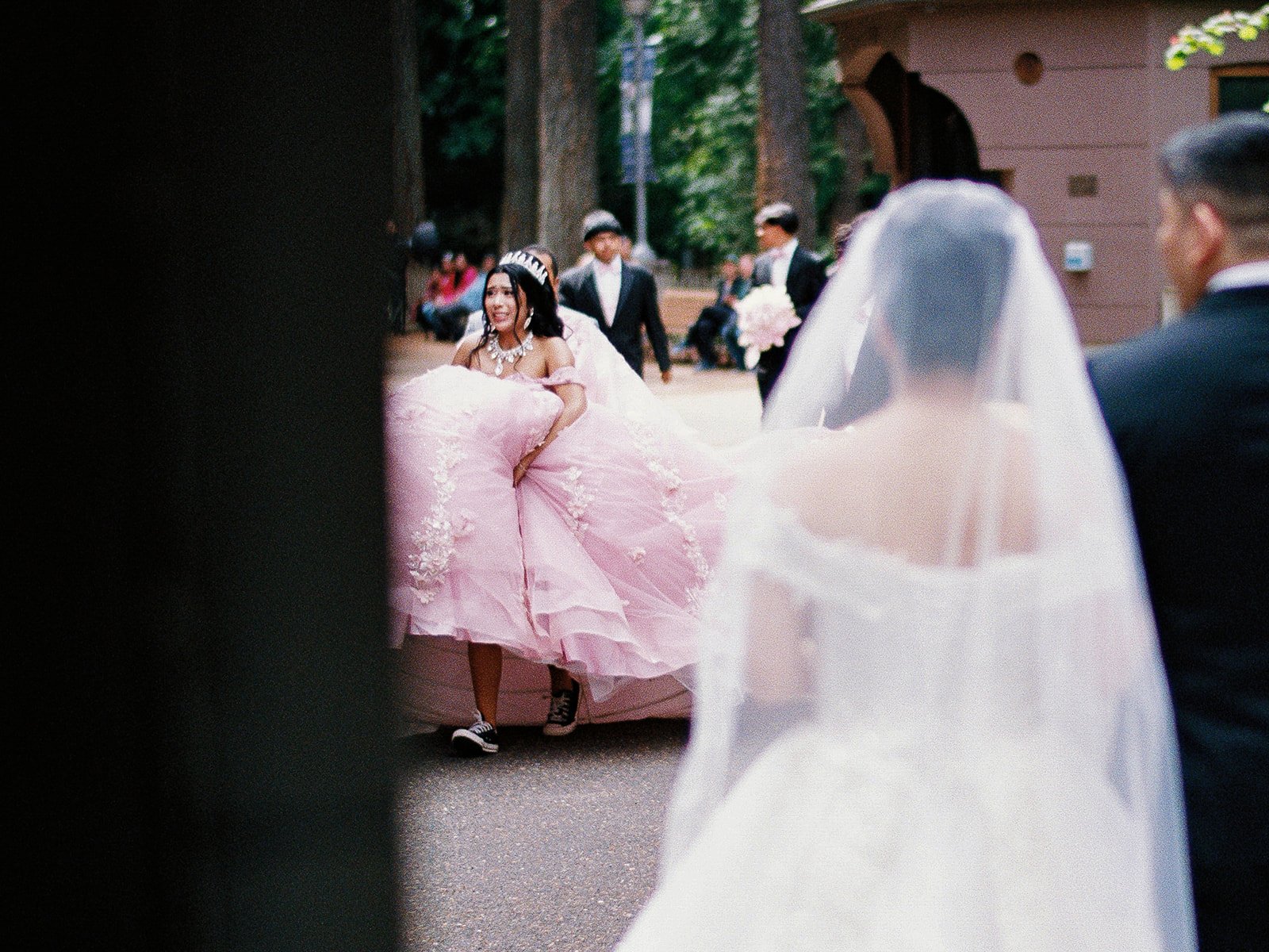 Quinceañera party carrying a large pink gown past a veiled bride waiting at The Grotto.