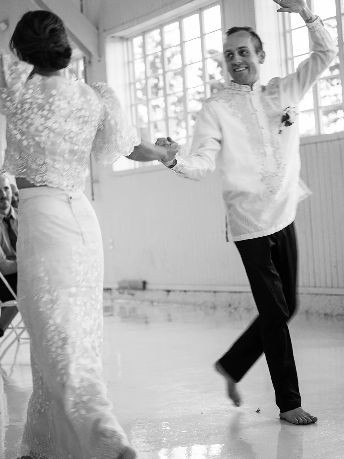 Black and white image of the groom dancing barefoot and exuberantly with the bride during their first dance inside the Pearson Air Museum hangar

