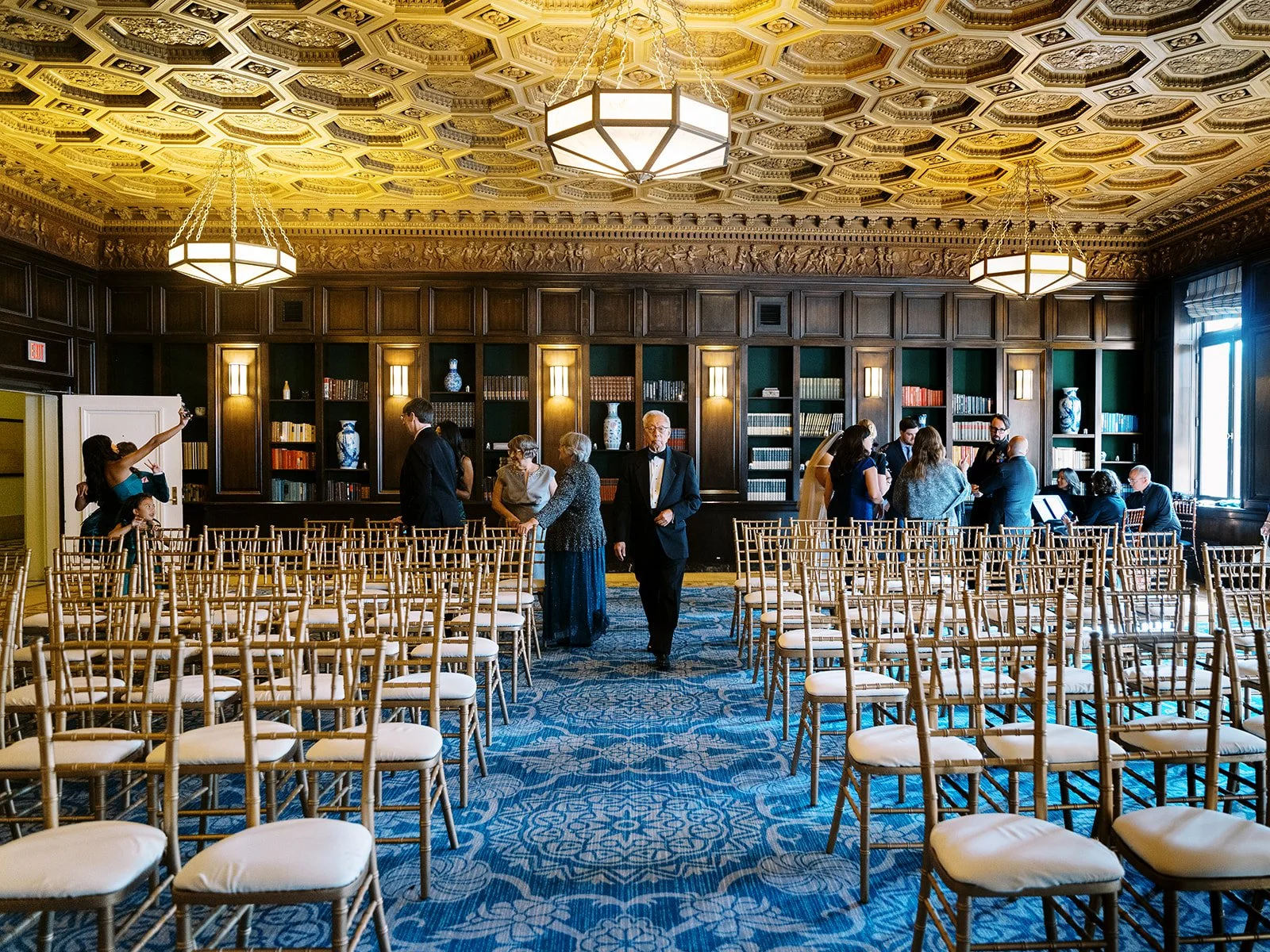 Wedding ceremony space with rows of gold chairs and guests gathering in an ornate library-style venue.
