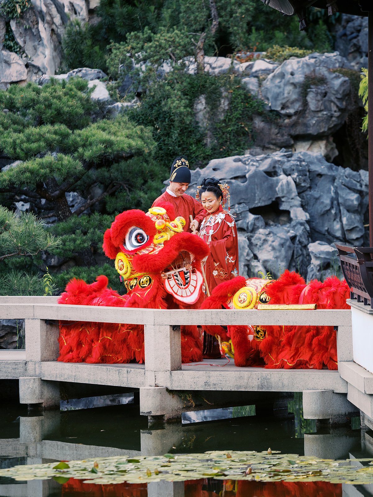 Couple in traditional red Chinese wedding attire with lion dancers at Portland’s Lan Su Chinese Garden.