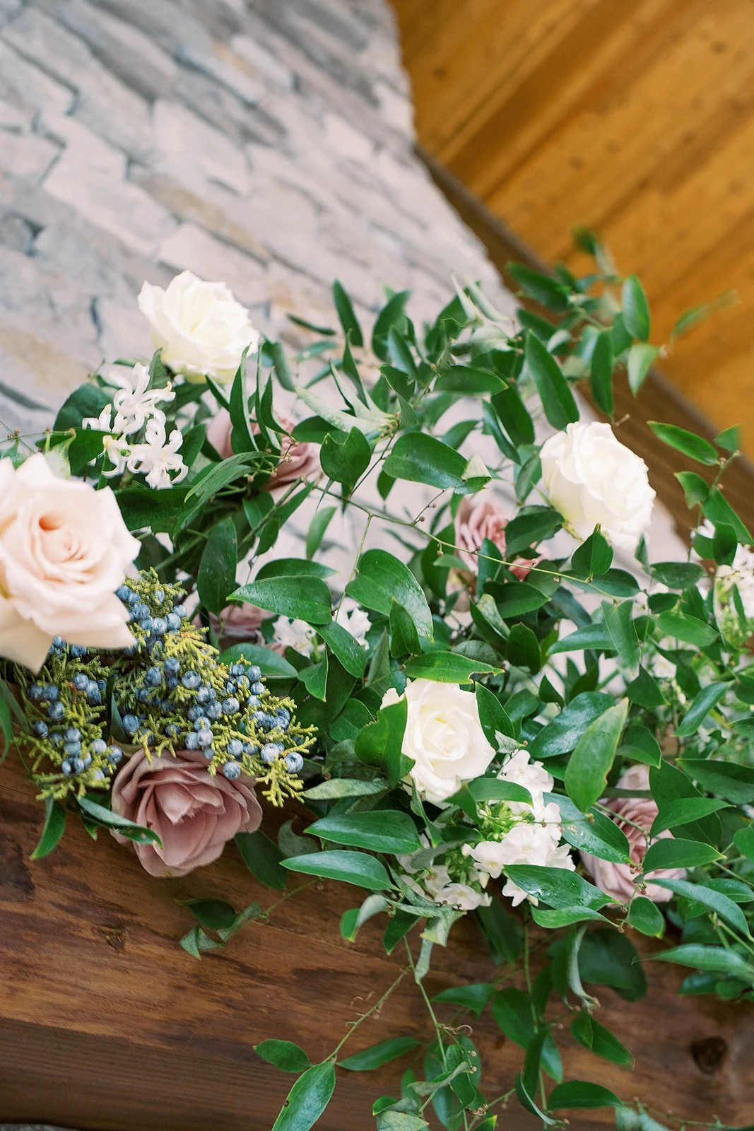 Close-up of blush and white roses with abundant greenery decorating the stone wedding fireplace.