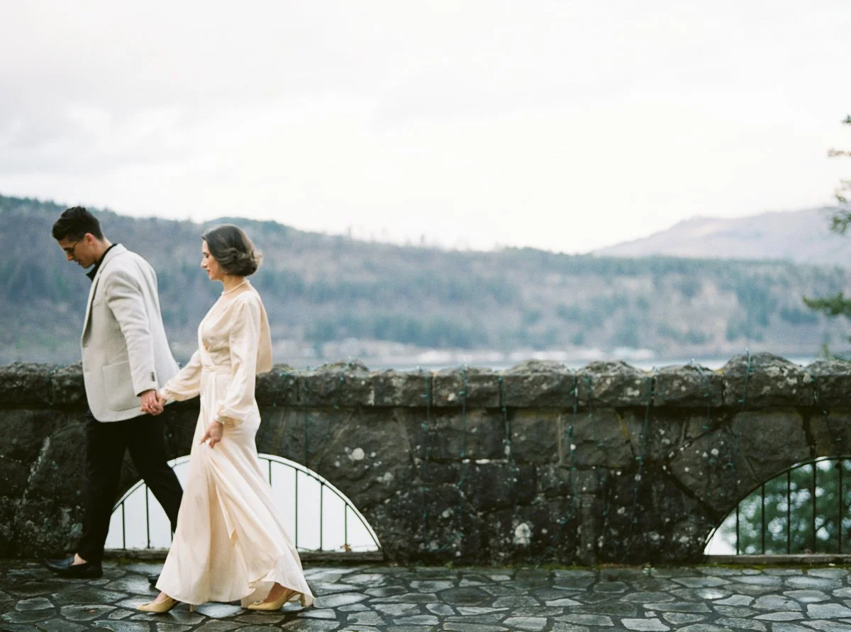 Couple holding hands along the cliffside terrace at Columbia Gorge Hotel, with the Columbia River in the background and a timeless, European-inspired aesthetic.