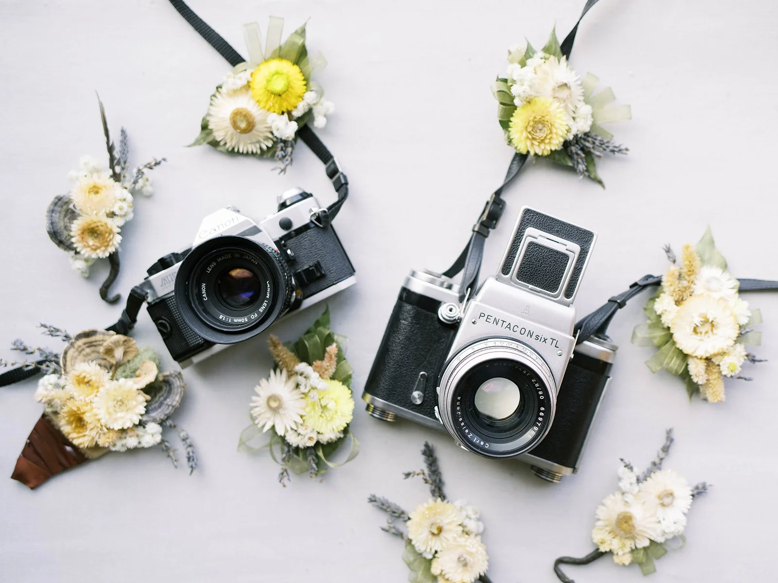 Two vintage film cameras surrounded by white and yellow wedding flowers and greenery.