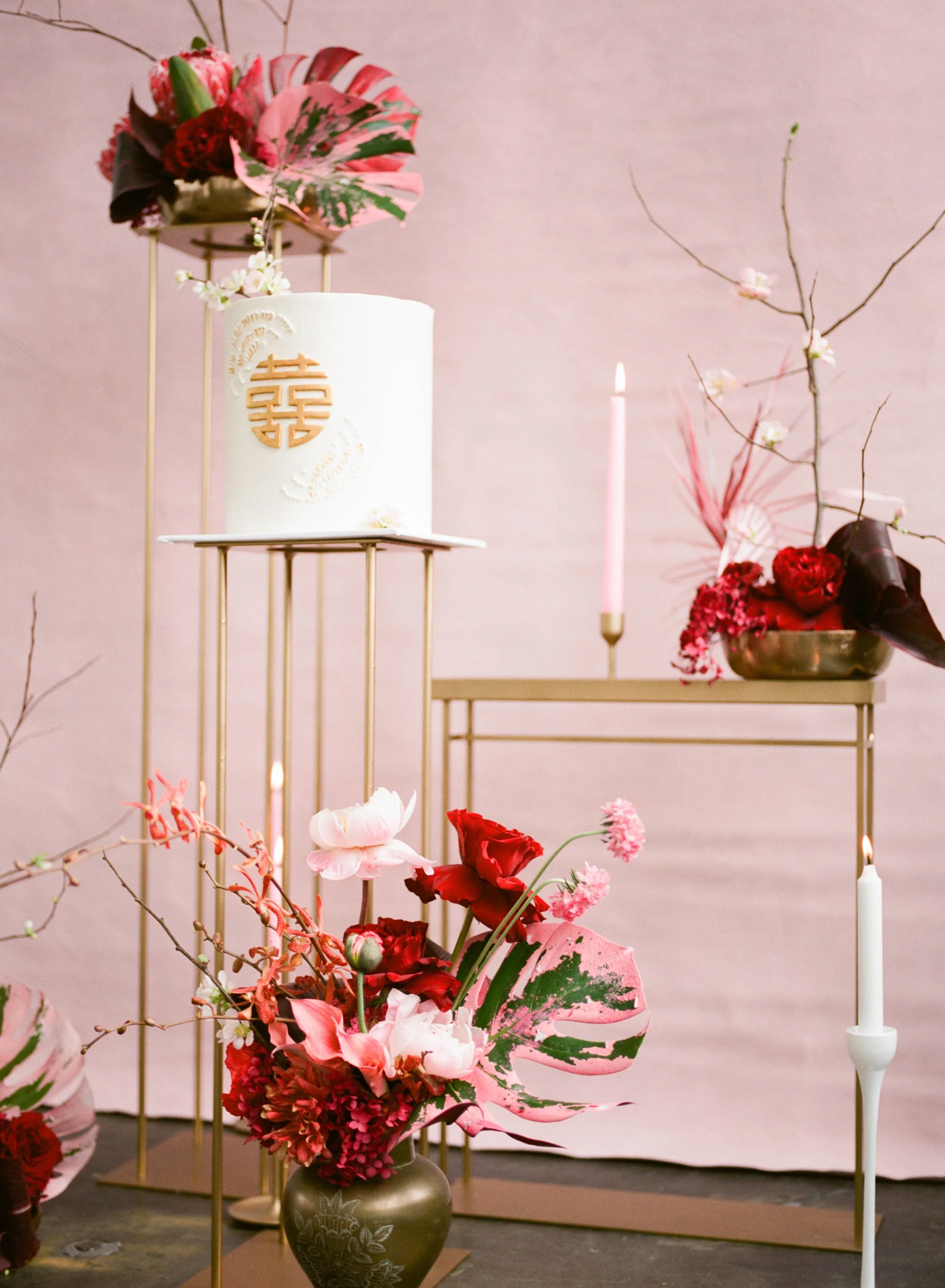 Lunar New Year wedding cake display with red and pink flowers, candles and gold accents.