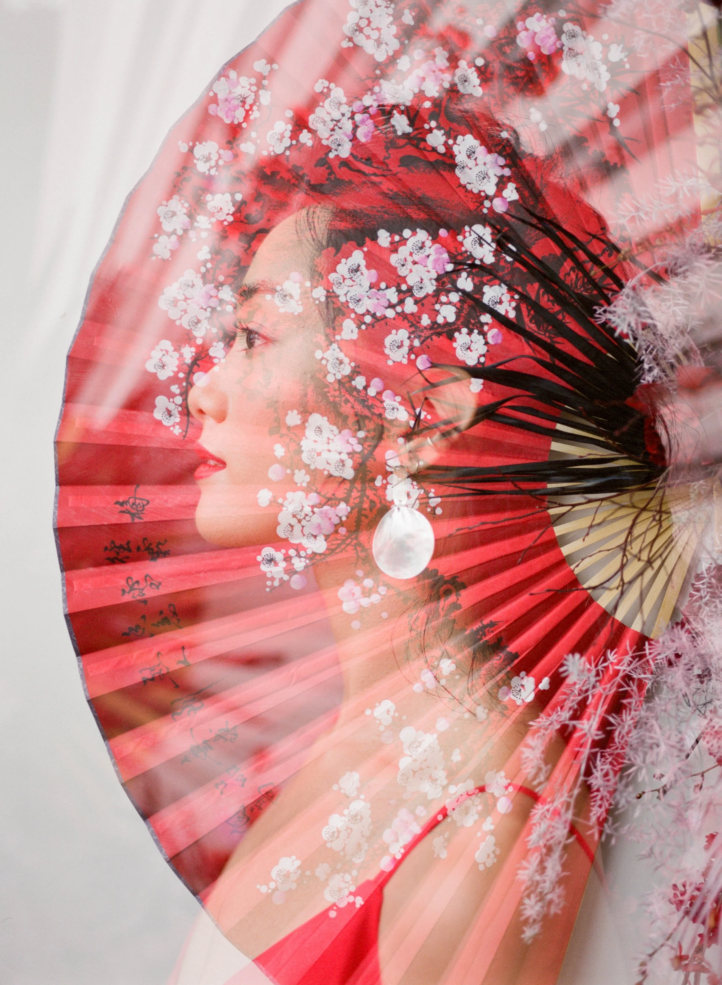 Double-exposure portrait of a woman framed by a red cherry blossom fan and soft floral details.